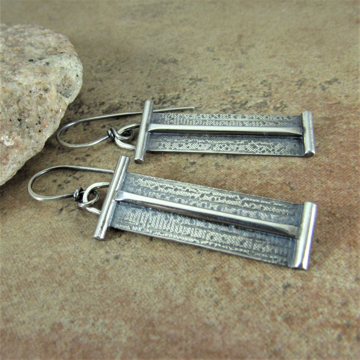 Pair of tabular shaped argentium silver earrings on a stone surface.