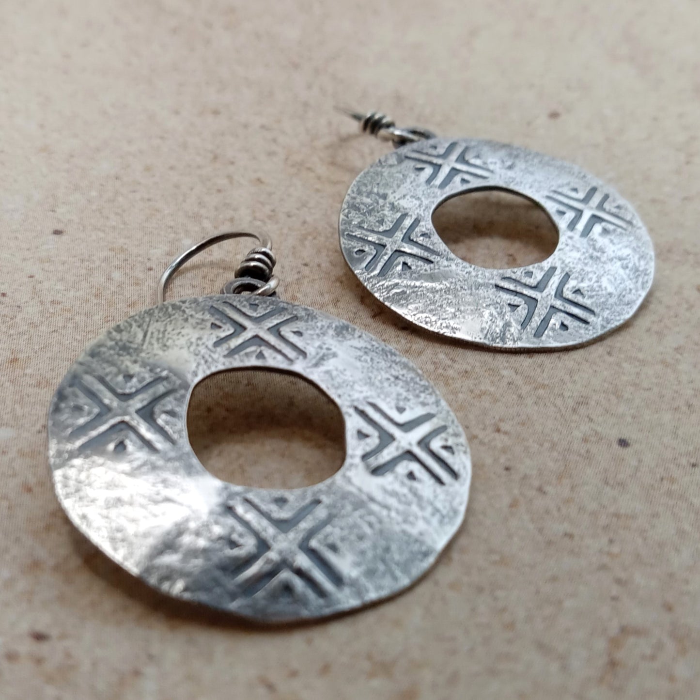 Ancient coin style earrings in SS by Mocahete, rustic texture, beige background.