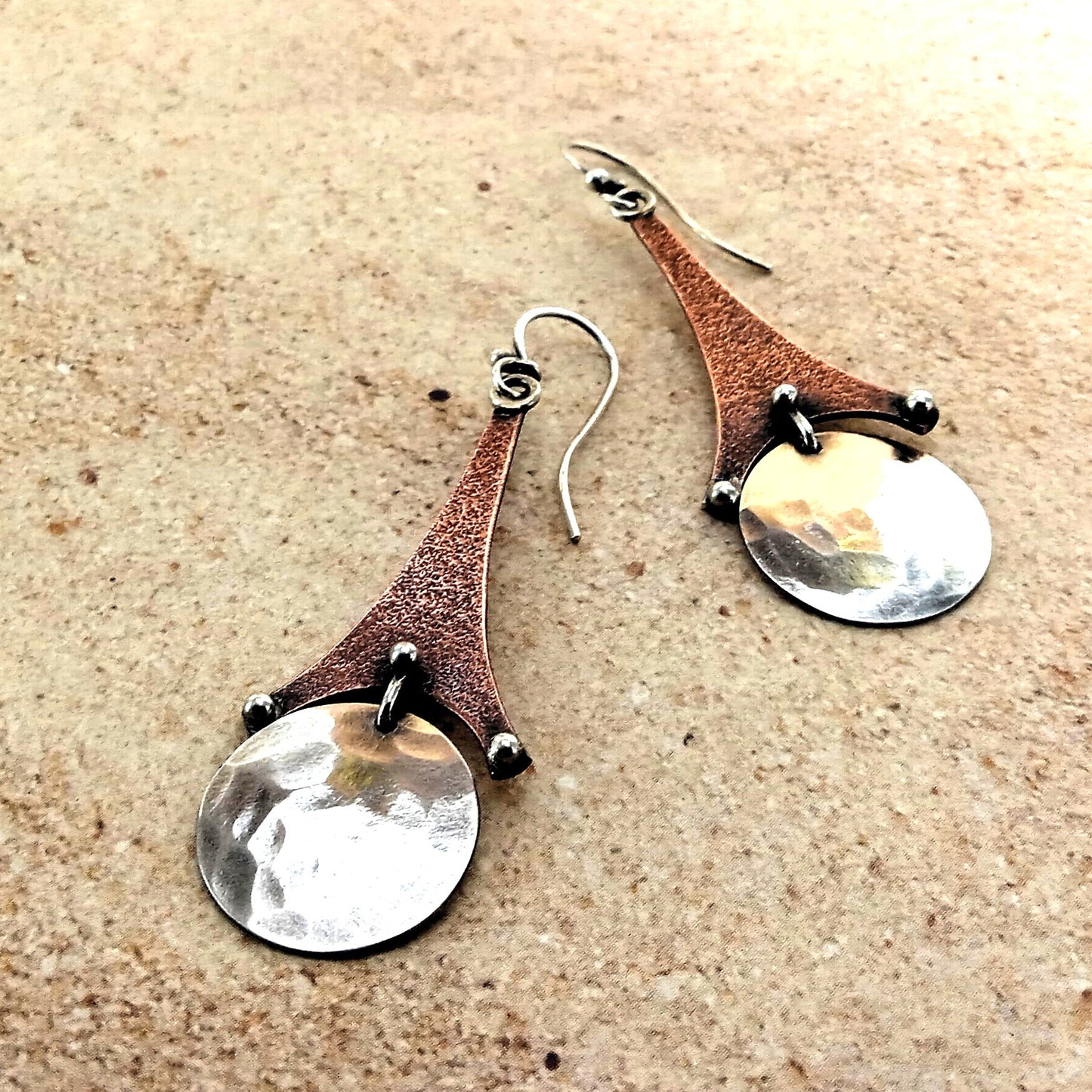Pair of mixed metal earrings with brown and silver components on a beige surface