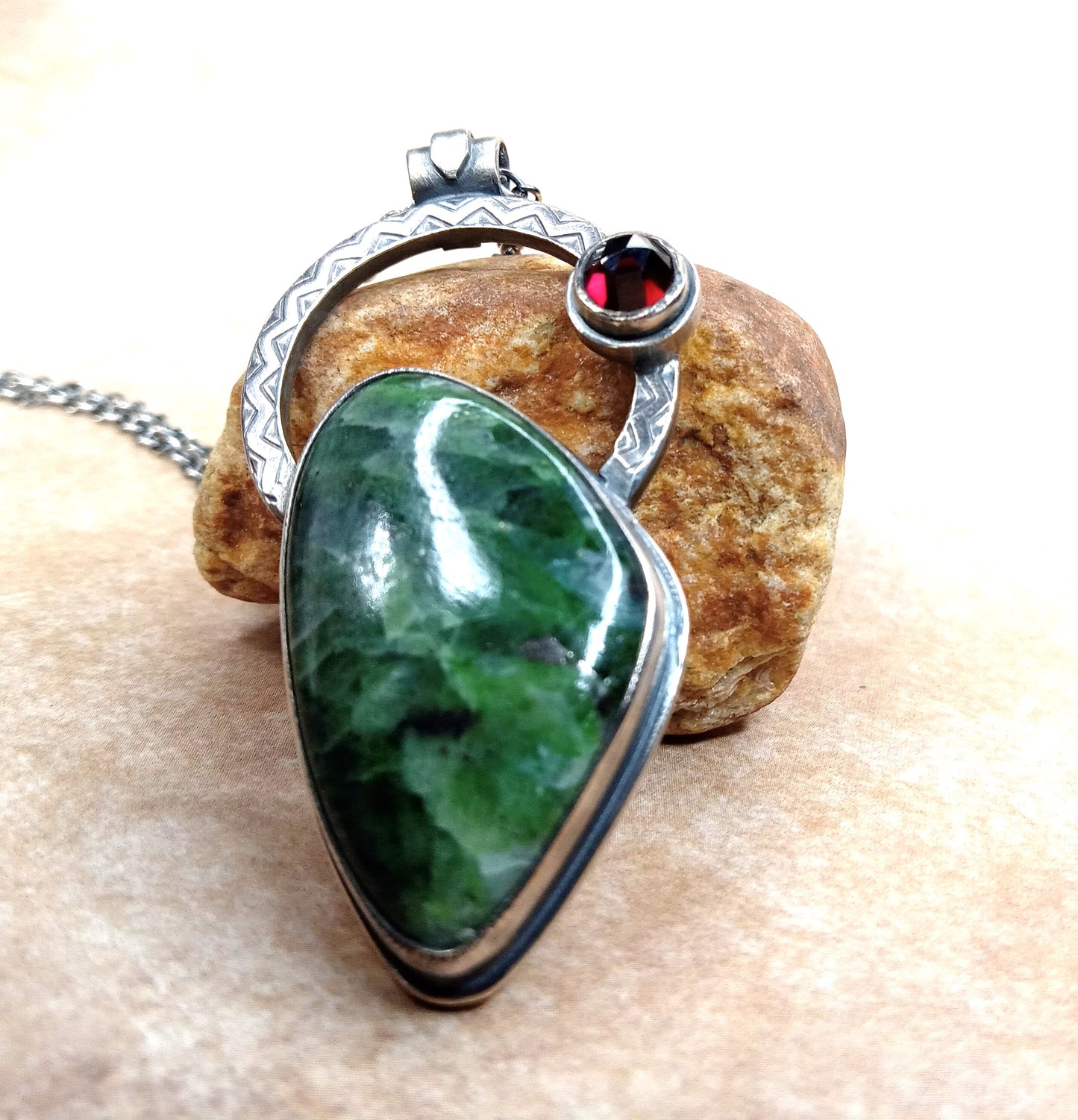 Green chrome diopside stone pendant with silver and red garnet gemstone on a rock.