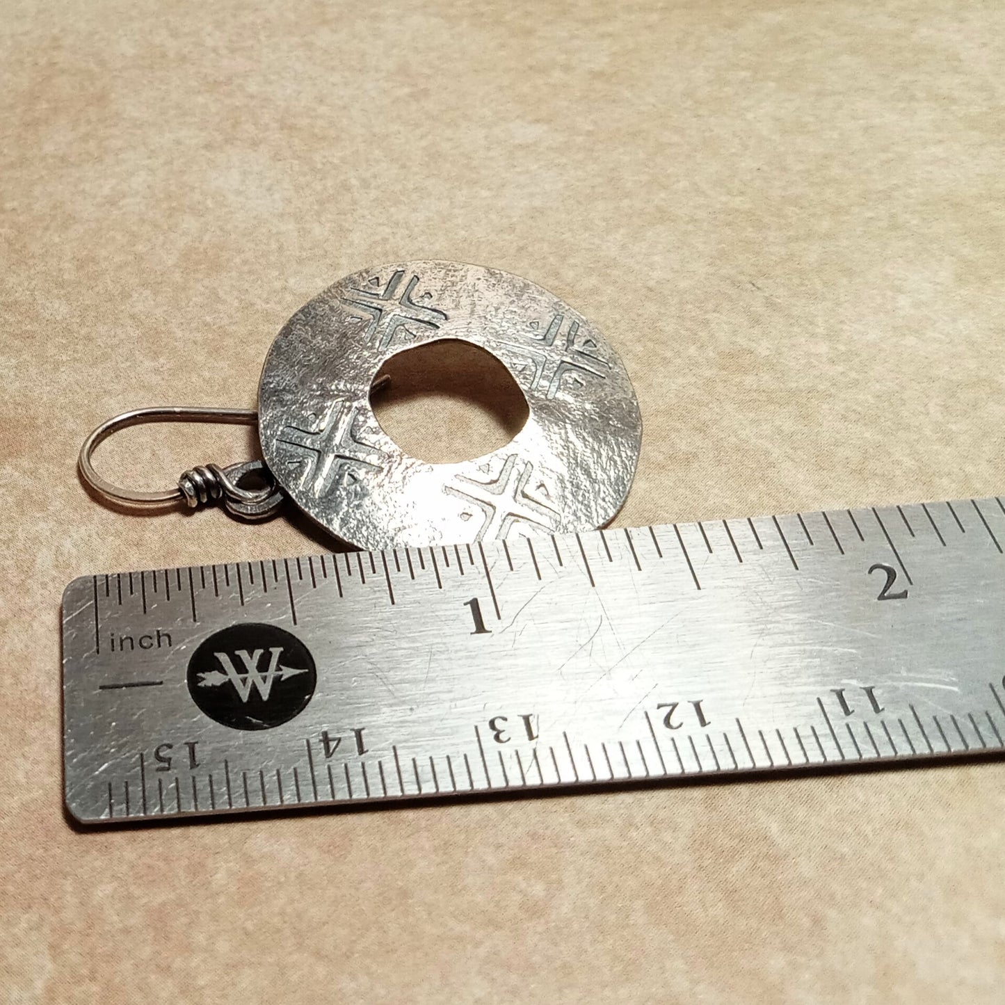 Sterling Silver rustic textured round earring next to a ruler on a beige background,