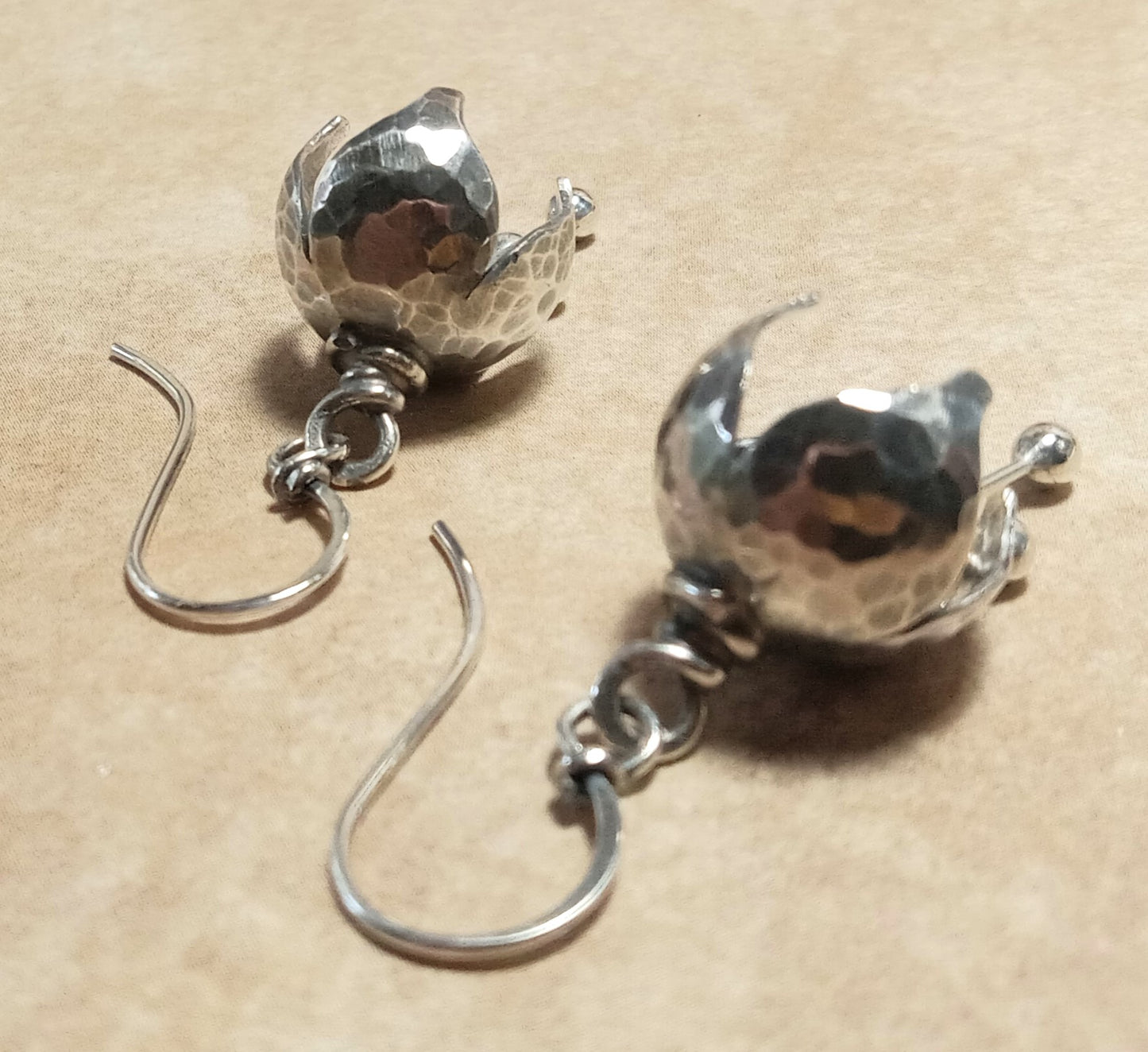 Pair of sterling silver bell shaped earrings on a beige background.