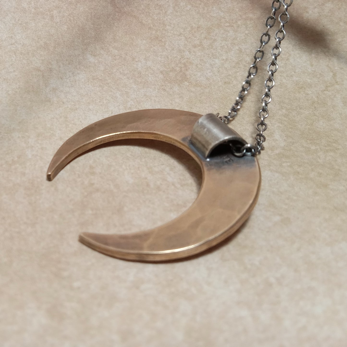 Backside of mixed metal crescent moon-shaped pendant on a chain against a beige background.