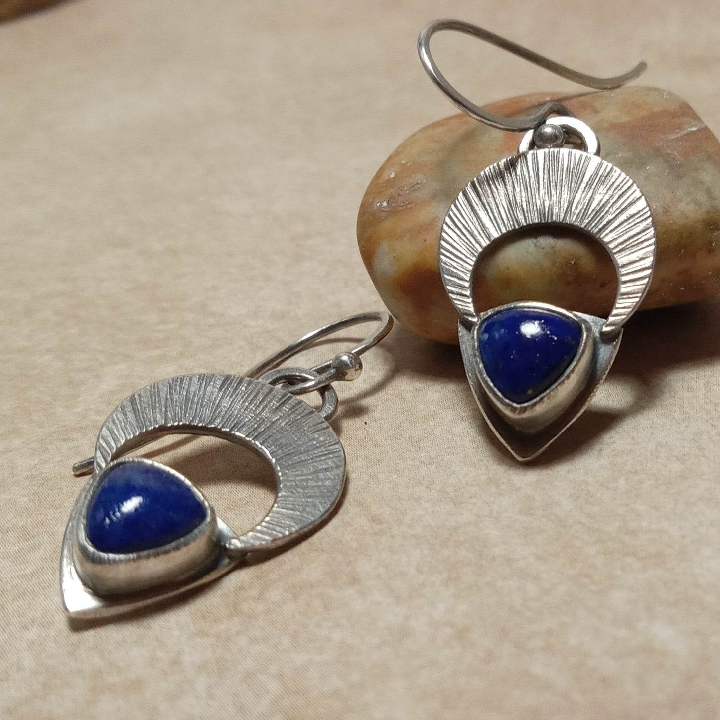 Argentium Silver crescent moon gemstone earrings with lapis lazuli stones on a beige surface with rock.