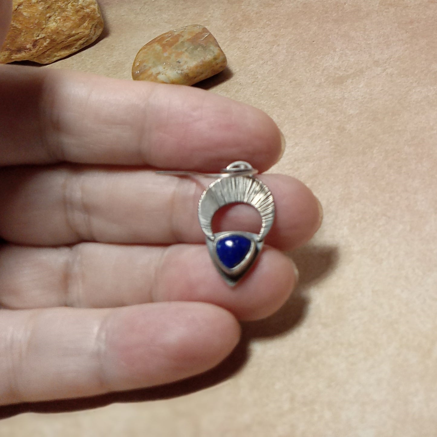 Silver and lapis earrings with crescent moon held between fingers on a beige background