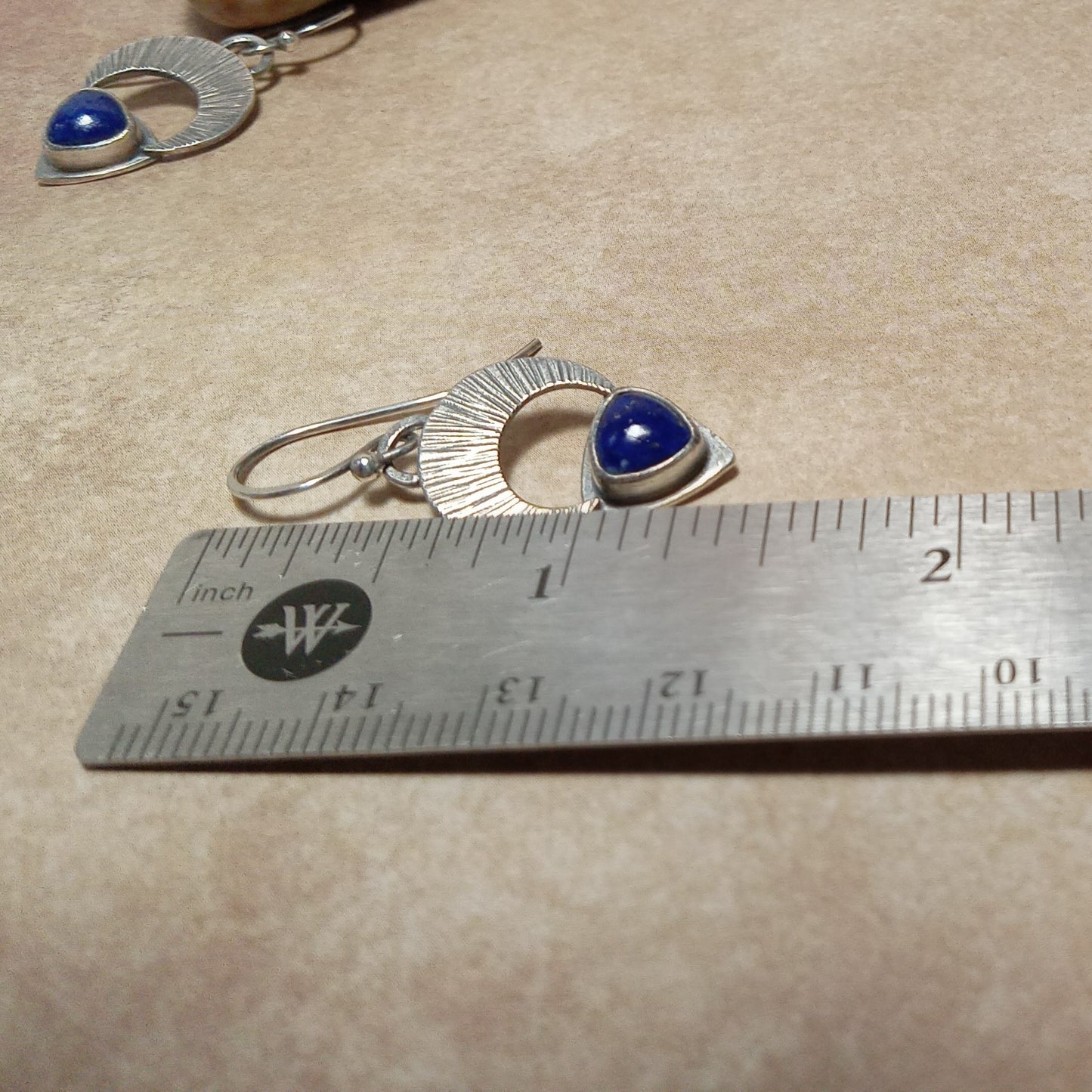 Argentium Silver earrings with blue lapis lazuli stones on a beige surface with a ruler for scale.
