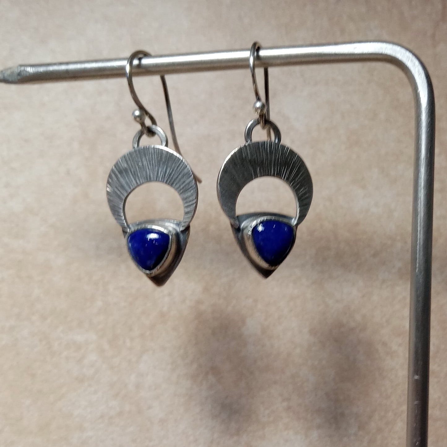 Argentium Silver earrings with lapis lazuli stones on a stand against a beige background.