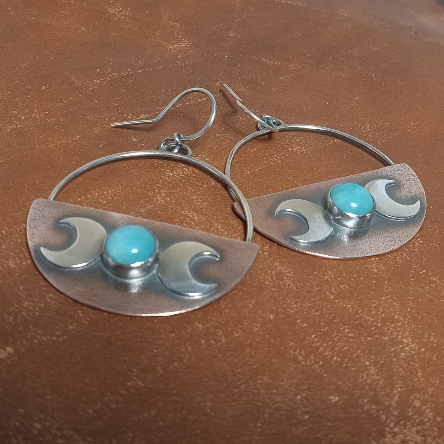 Front view of Amazonite, copper and sterling silver triple goddess earrings by Mocahete photographed on brown leather.