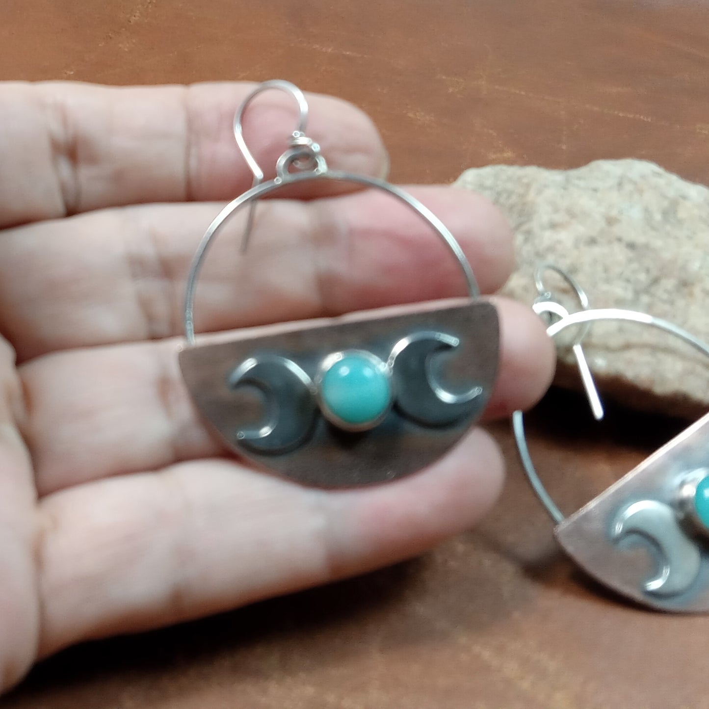 Copper and Silver earrings with amazonite stones held in a hand on a leather and rock surface.