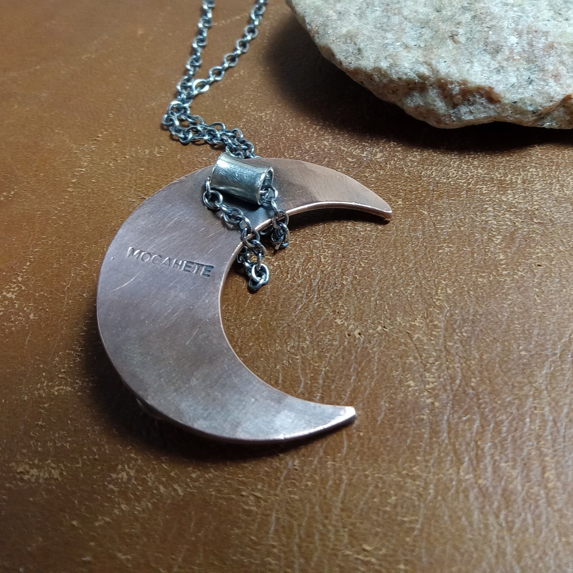 Reverse side of copper and Silver crescent moon necklace on a brown surface showing "Mocahete" makers mark.