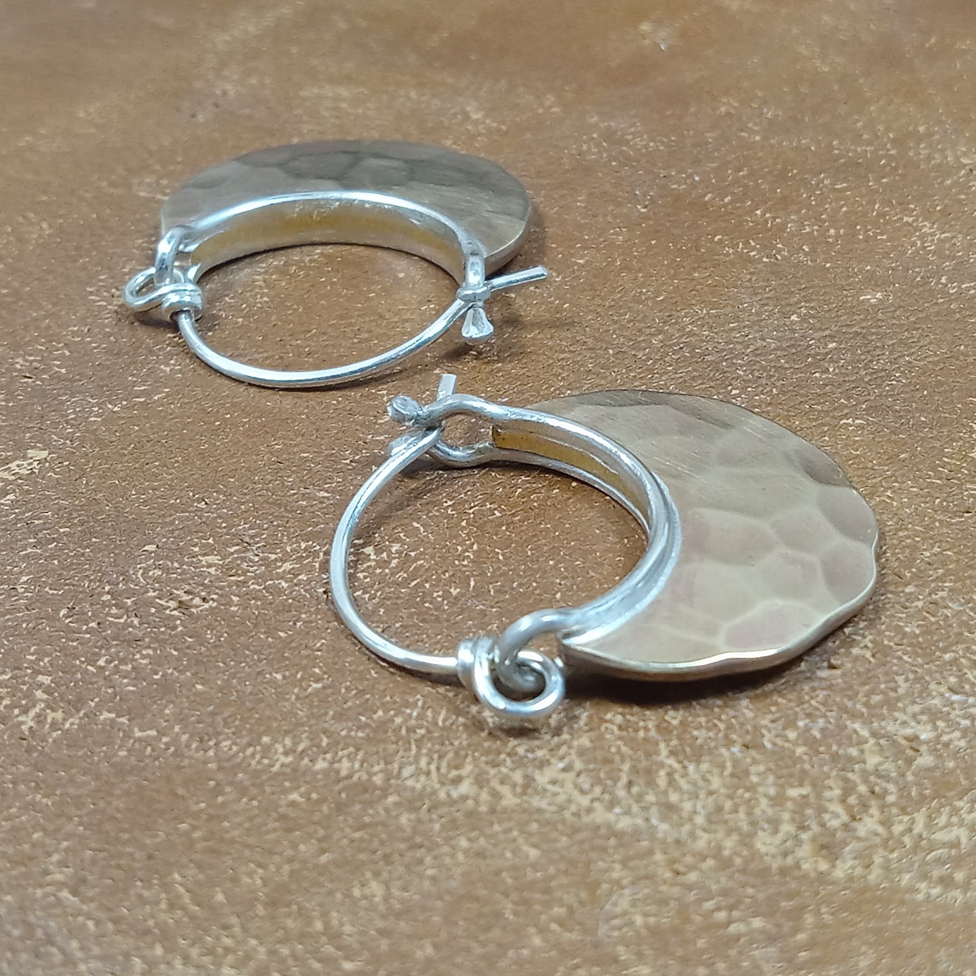 pair of bronze and sterling silver small hoop earrings with friction clasp on brown background.