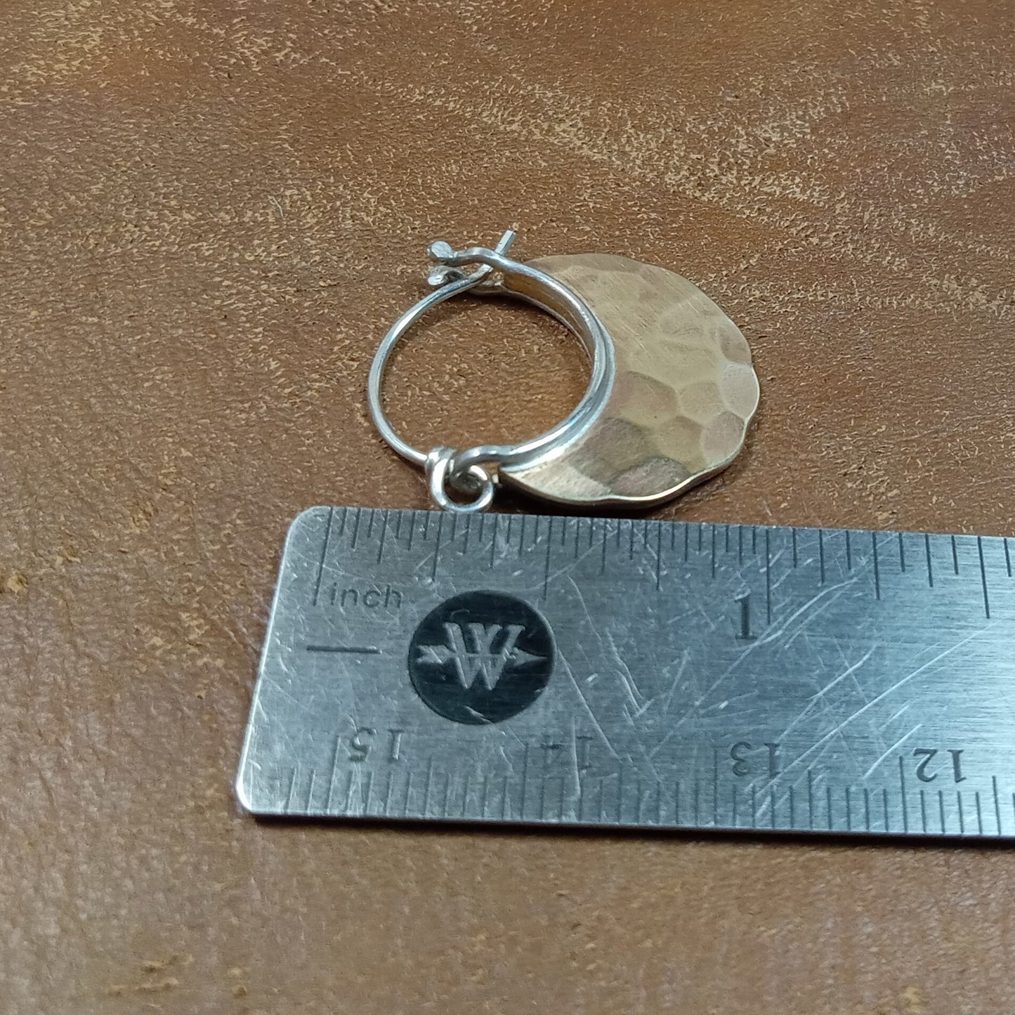 Bronze and SS hoop earring next to a ruler on a brown surface.
