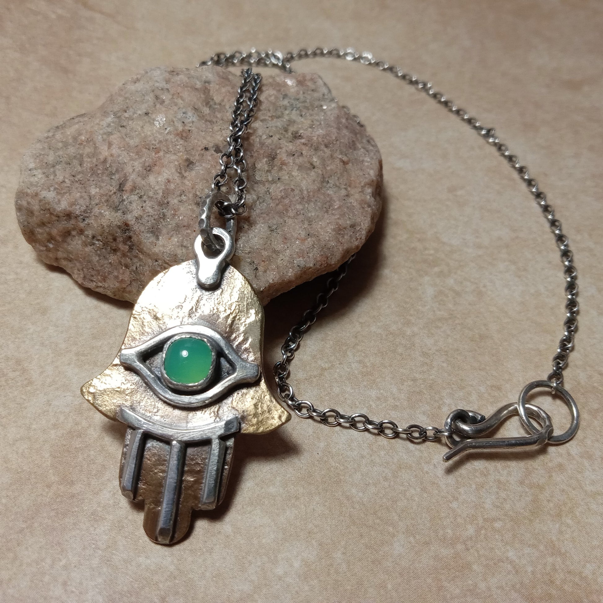 Hamsa Necklace by Mocahete with eye-shaped design with chrysoprase on a stone surface.