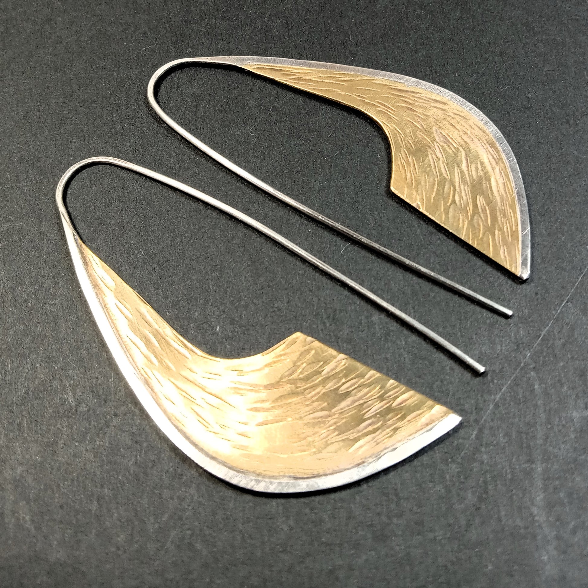 Pair of bronze and silver statement earrings by Mocahete on a dark surface