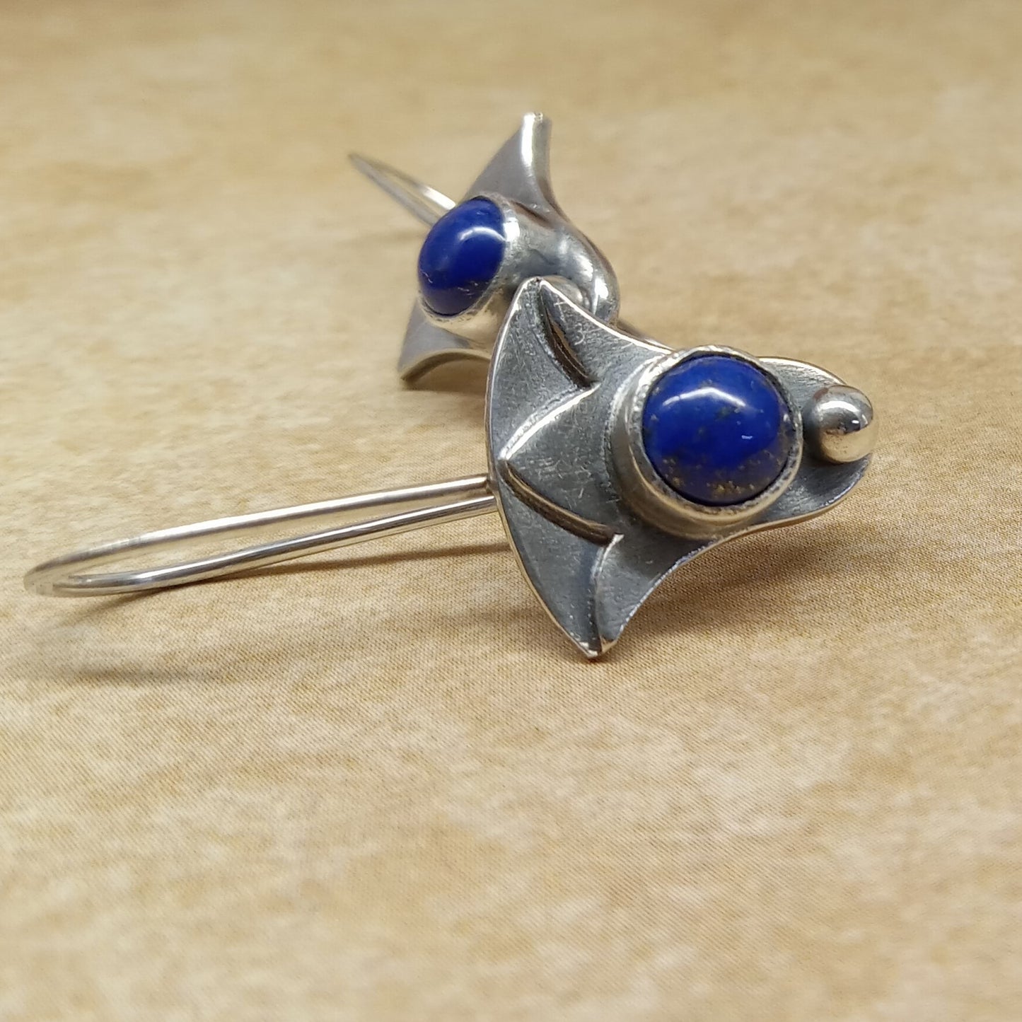 Side view of Argentium and lapis lazuli lotus earrings by Mocahete on beige background