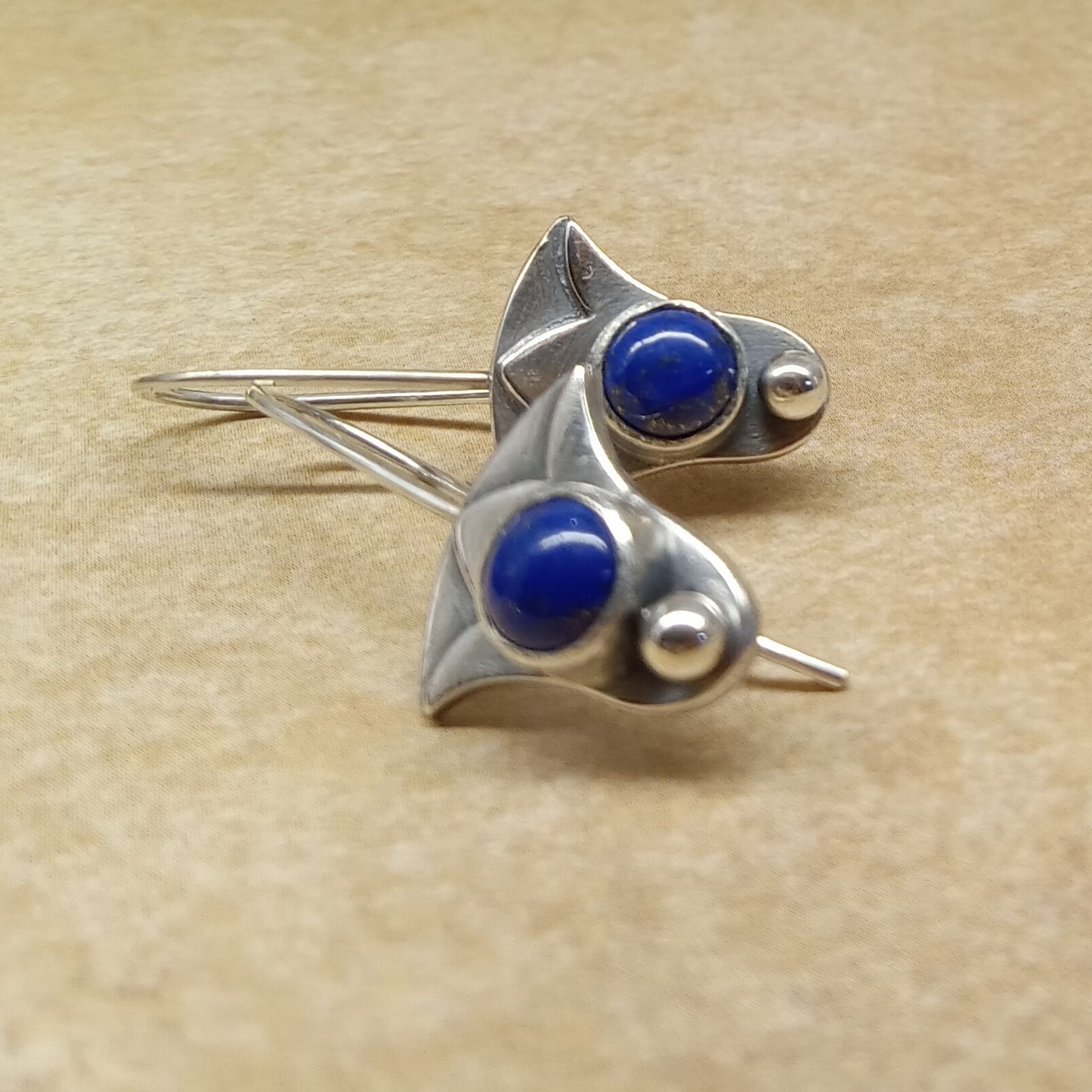 Pair of  lapis lazuli lotus earrings showing layered silver design and polished sphere accent on beige background