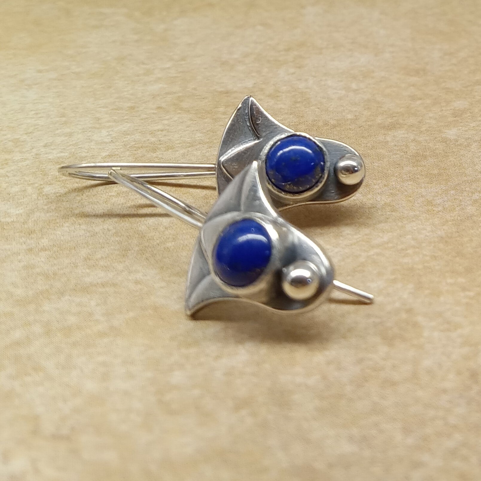 Pair of  lapis lazuli lotus earrings showing layered silver design and polished sphere accent on beige background