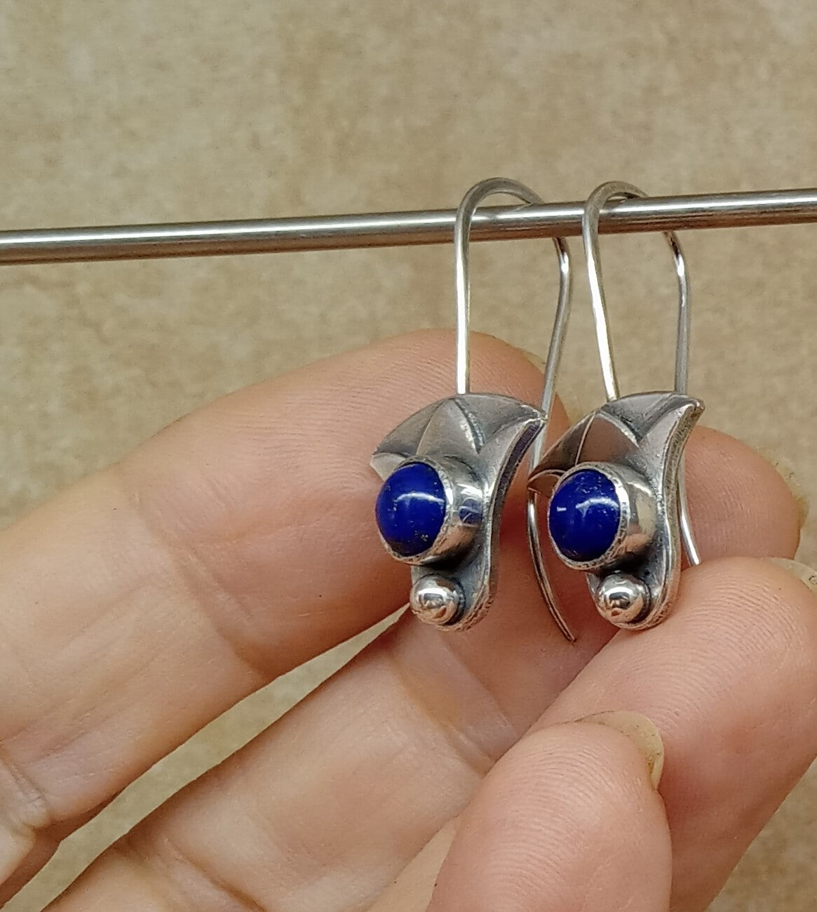 Argentium Silver earrings with blue lapis stones held by a hand against a beige background