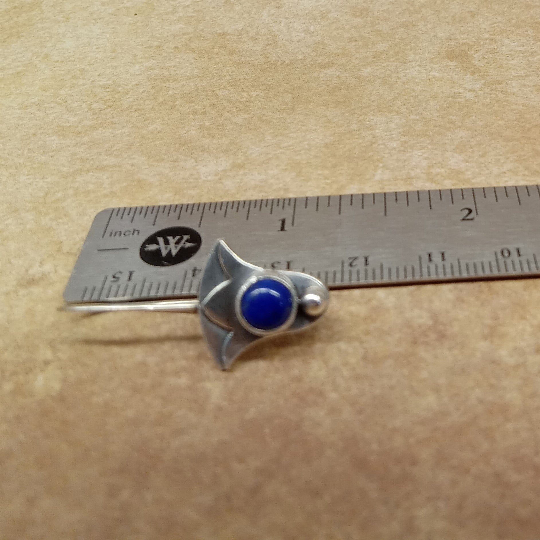 Silver lotus earrings with lapis gemstone on a beige background with a ruler for scale.