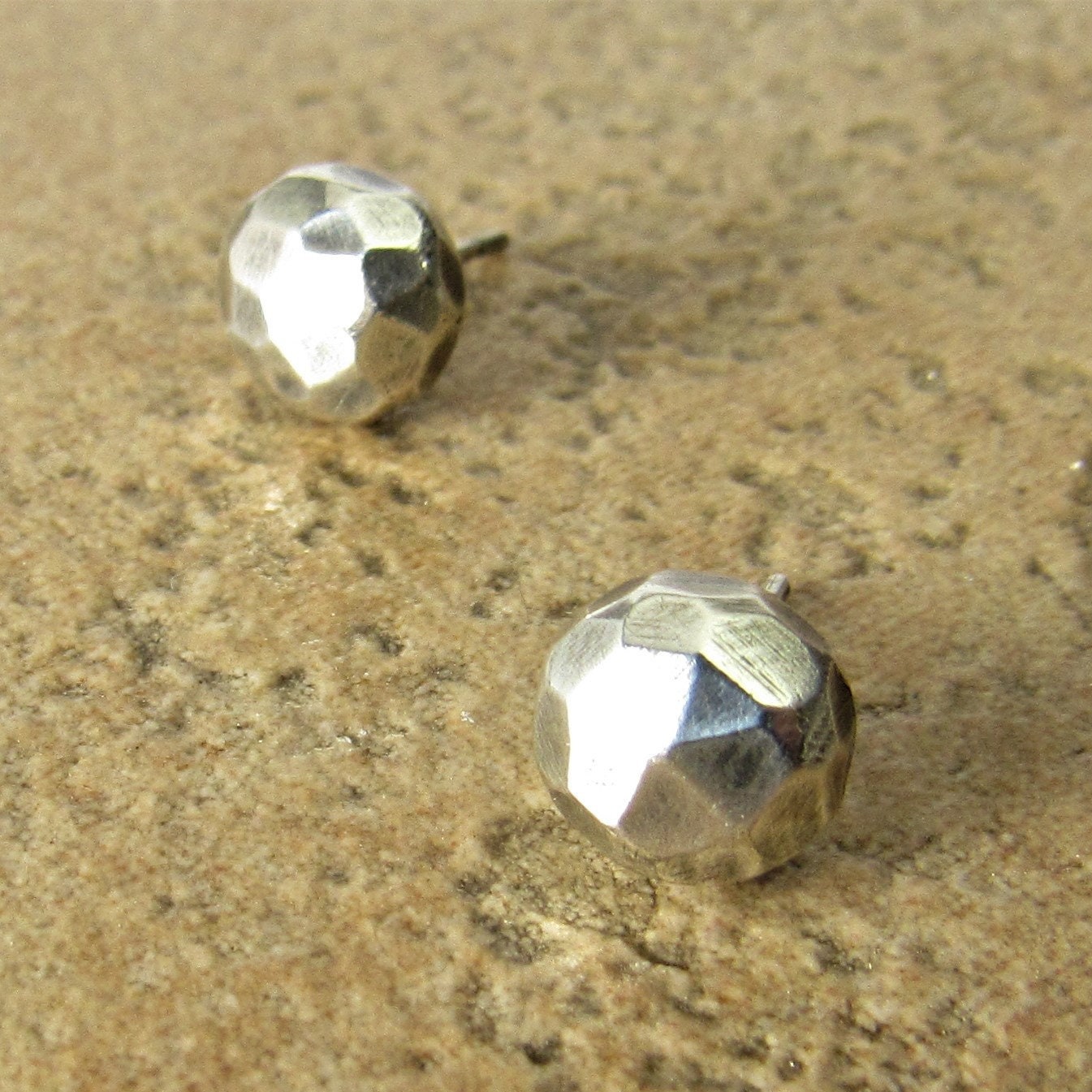 Faceted sterling silver nugget stud earrings with oxidized finish and sterling silver backs on textured beige background.