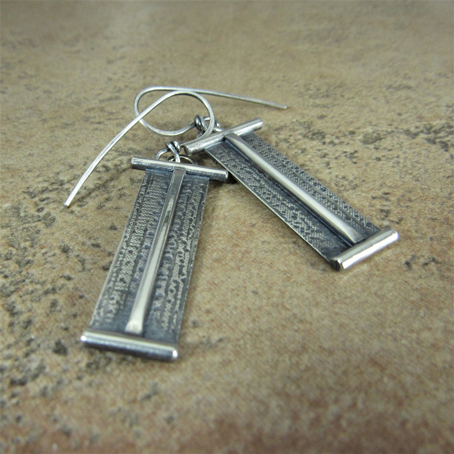 Pair of rectangular silver earrings on a textured surface.