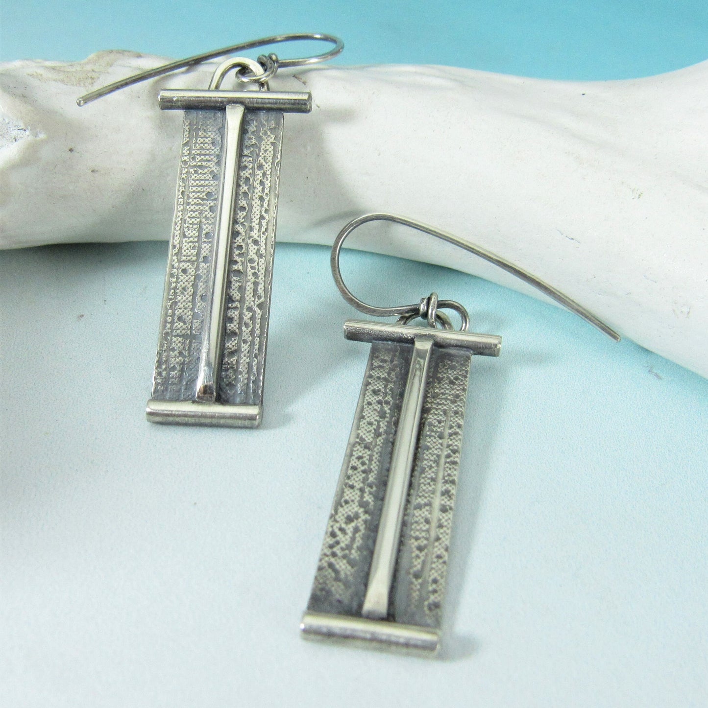 Silver earrings with vertical patterns on a light blue surface