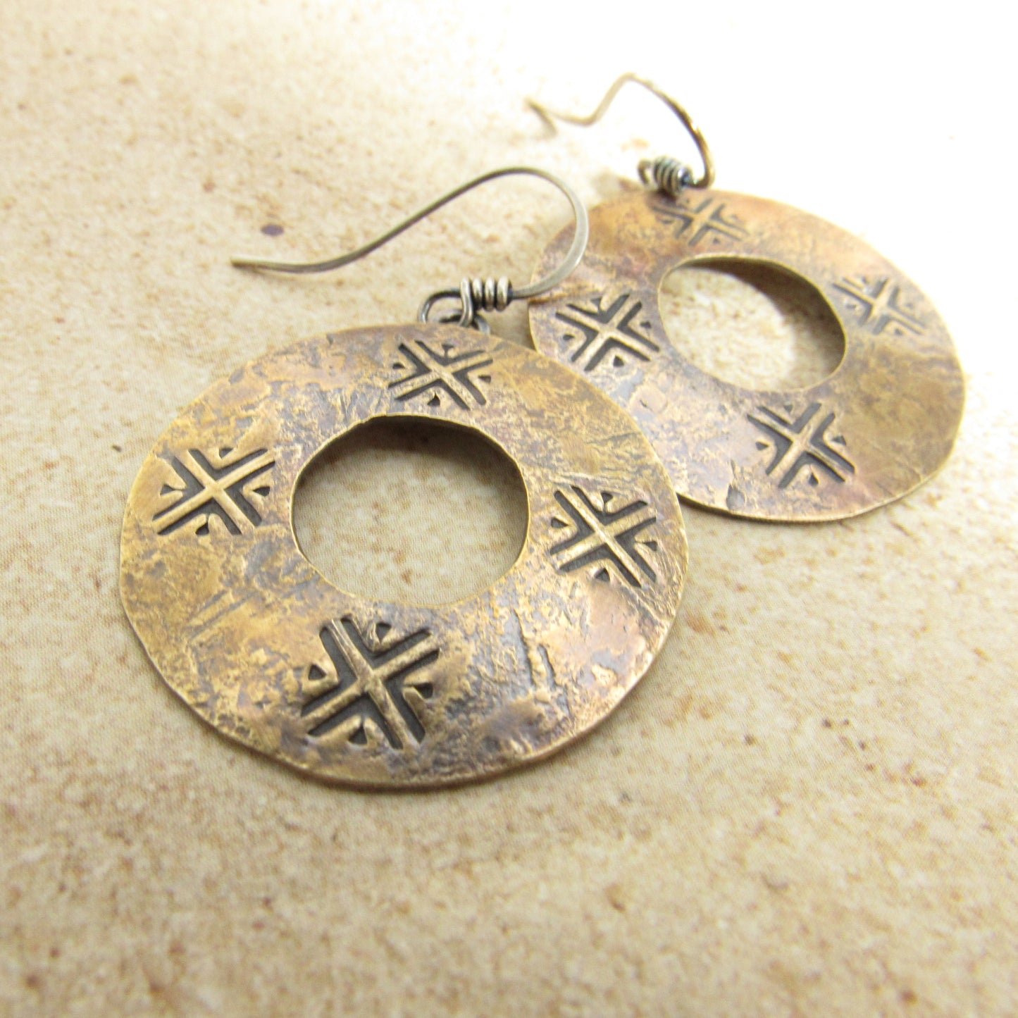 Pair of gold color ancient coin style earrings with intersting designs on a beige background