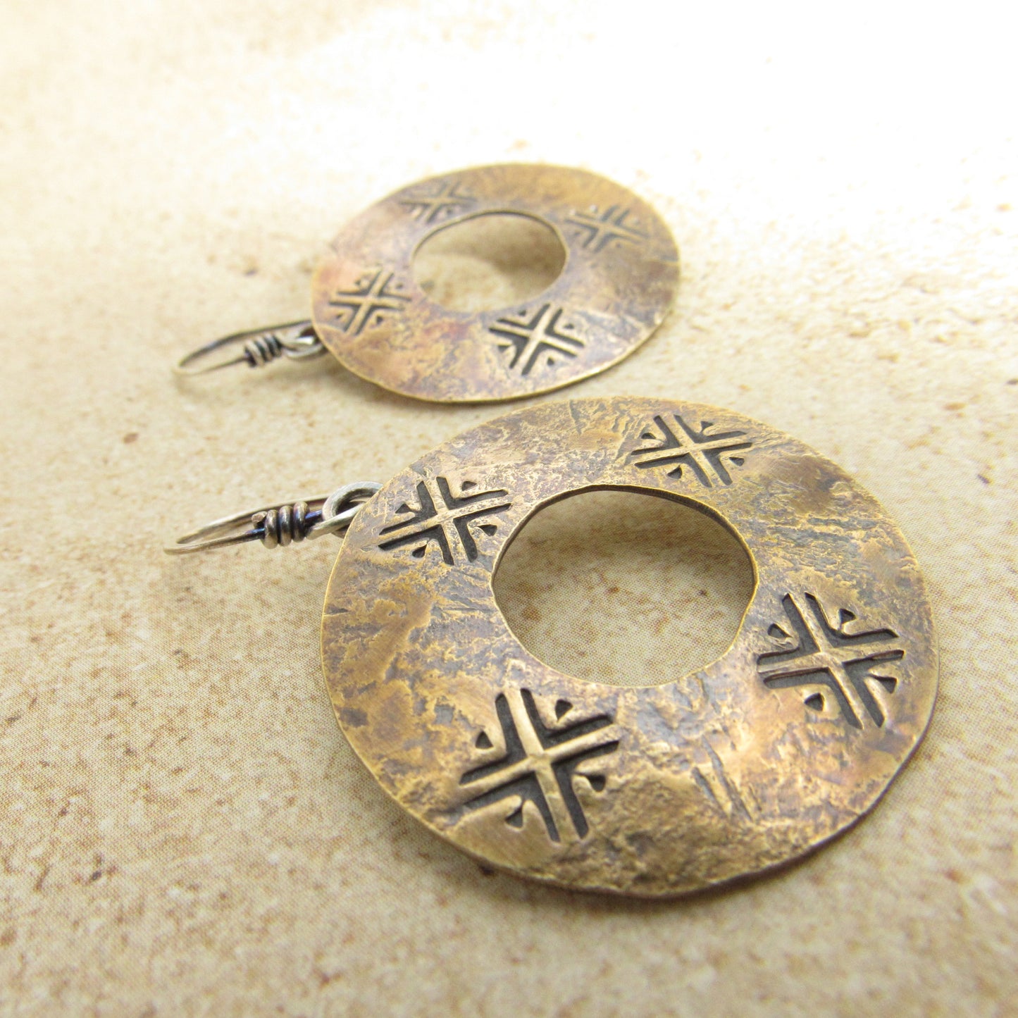 Pair of bronze earrings with hand stamped designs on a beige surface