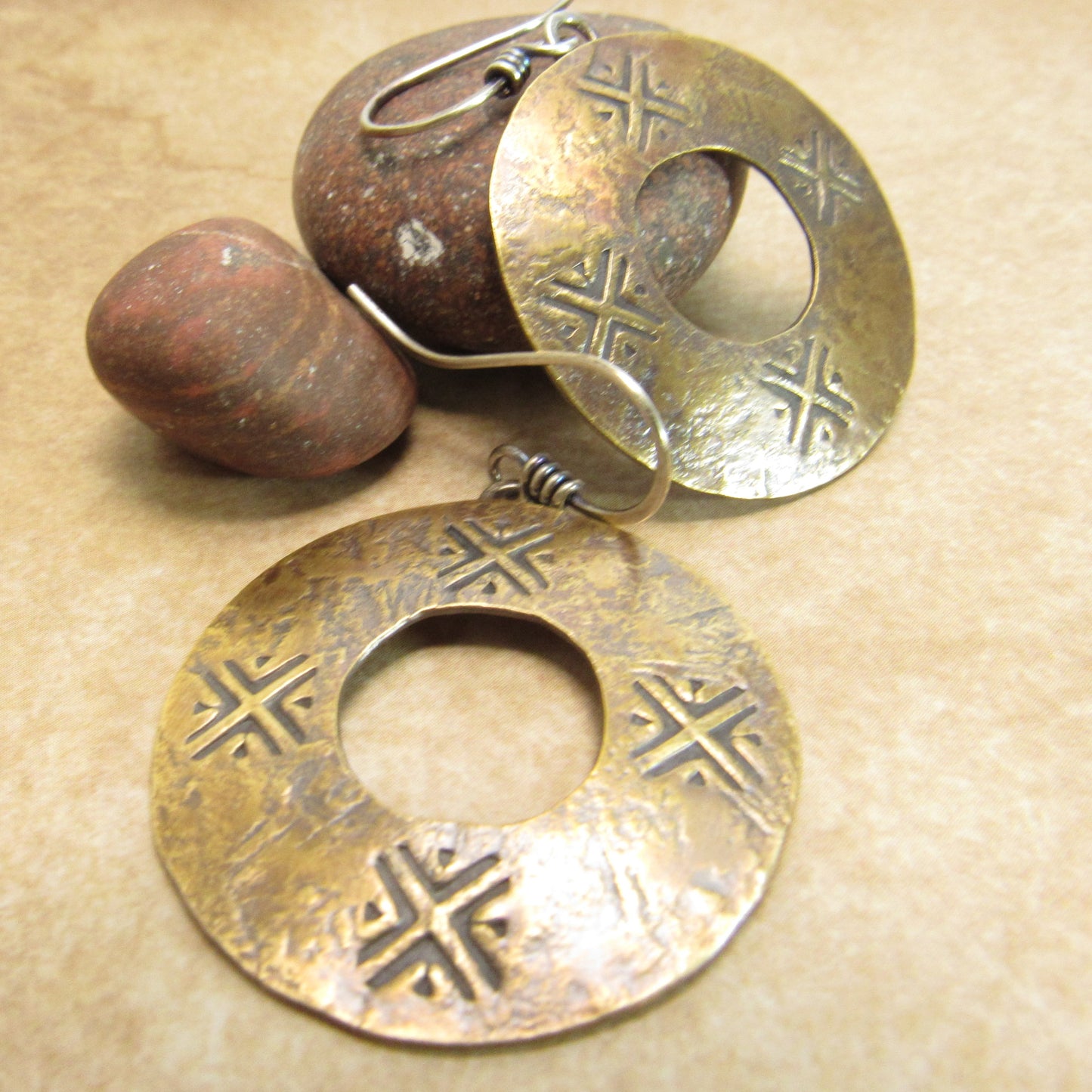Pair of bronze earrings ancient style coin with intricate designs on a beige background with rocks