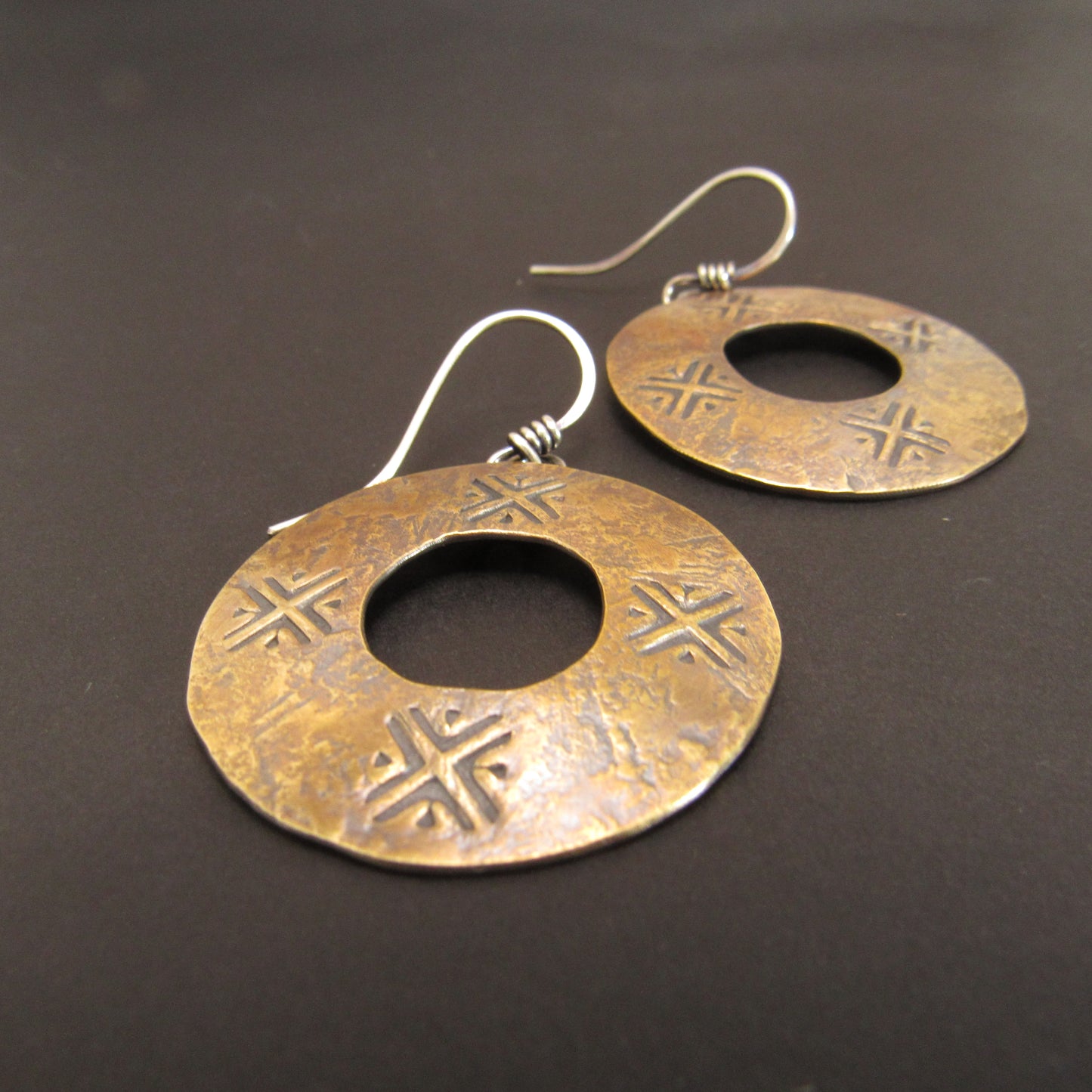 Pair of gold color dangle hoop earrings with stamped pattern on a dark background