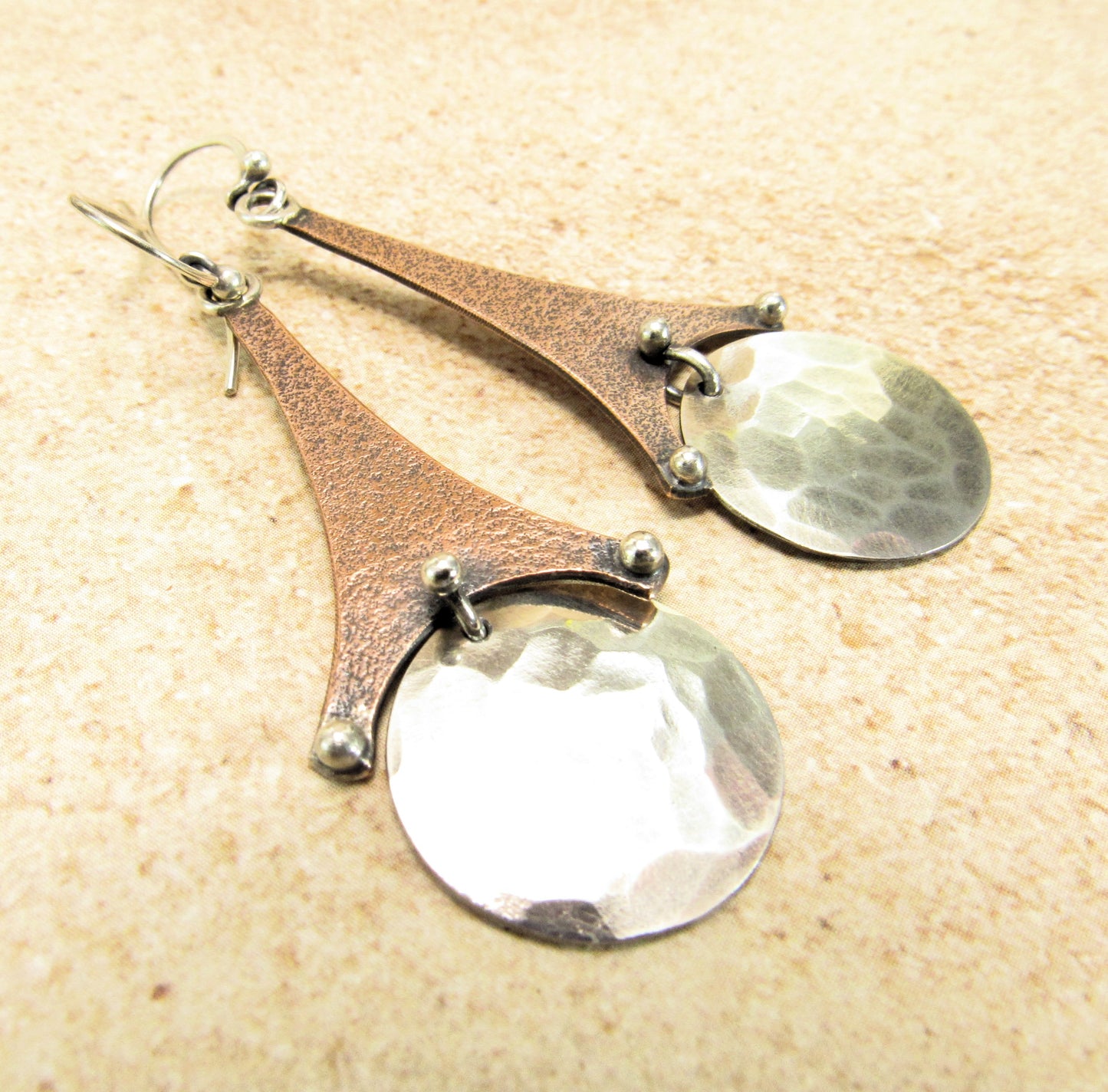Kinetic mixed metal earrings by Mocahete on beige background.