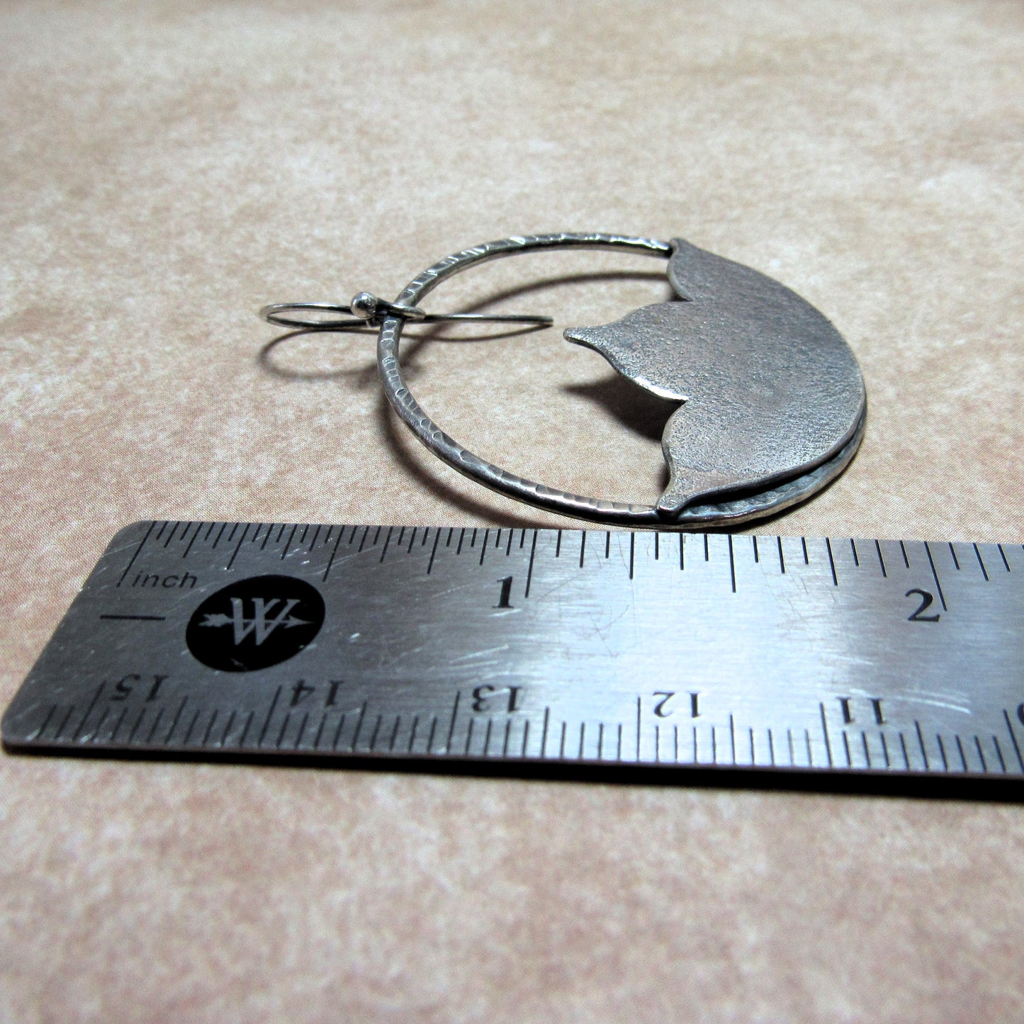 SS large lotus shape earrings next to a ruler on a beige surface.