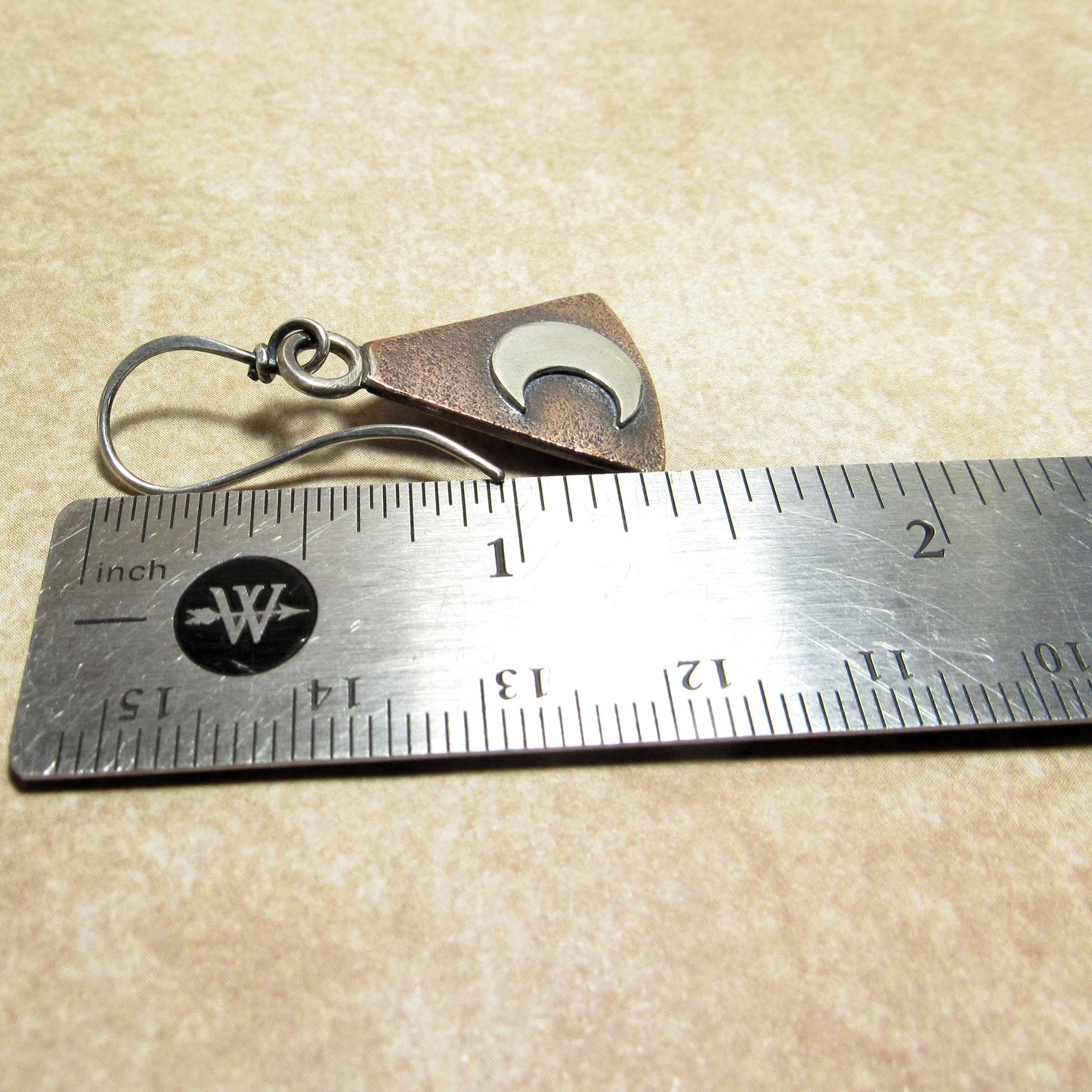 Mixed metal moon earring next to a ruler on a beige background