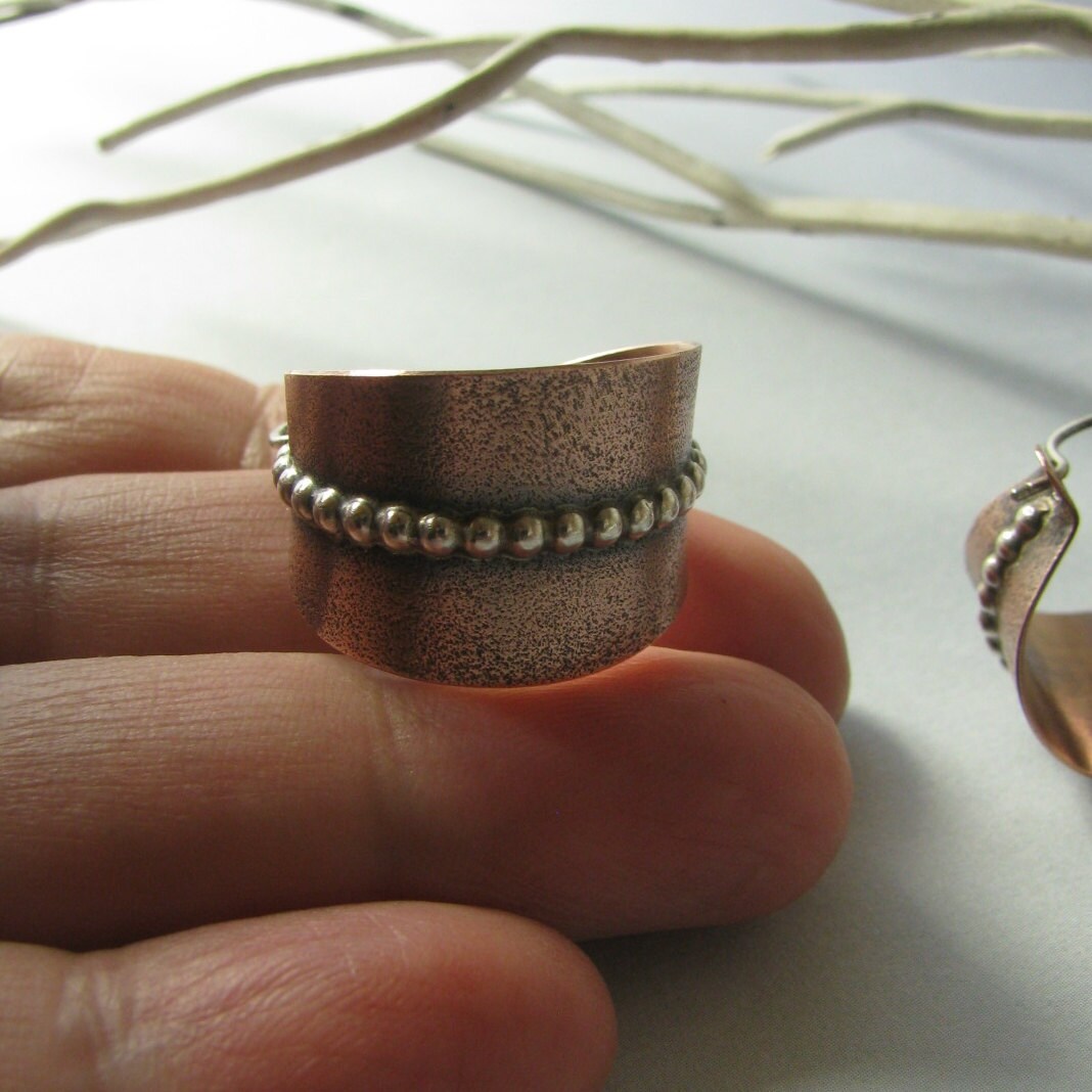 Copper and silver earrings with beaded detail on hand against a neutral background.