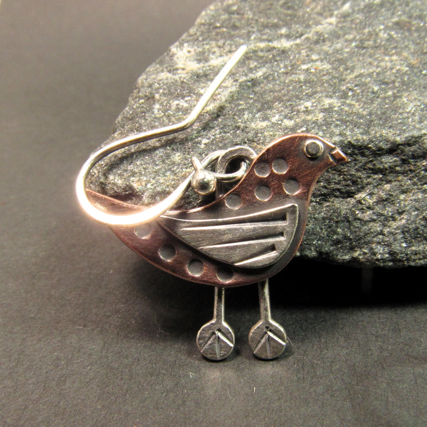 Lightweight boho-style bird earrings in copper and Argentium sterling silver, handmade with intricate detailing. On dark background with rock.