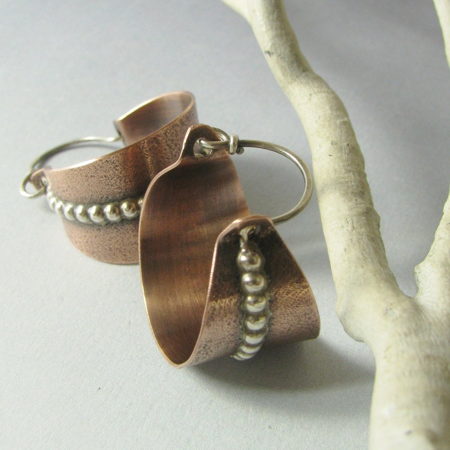 Copper earrings with bead detailing on a light gray background with white branch.