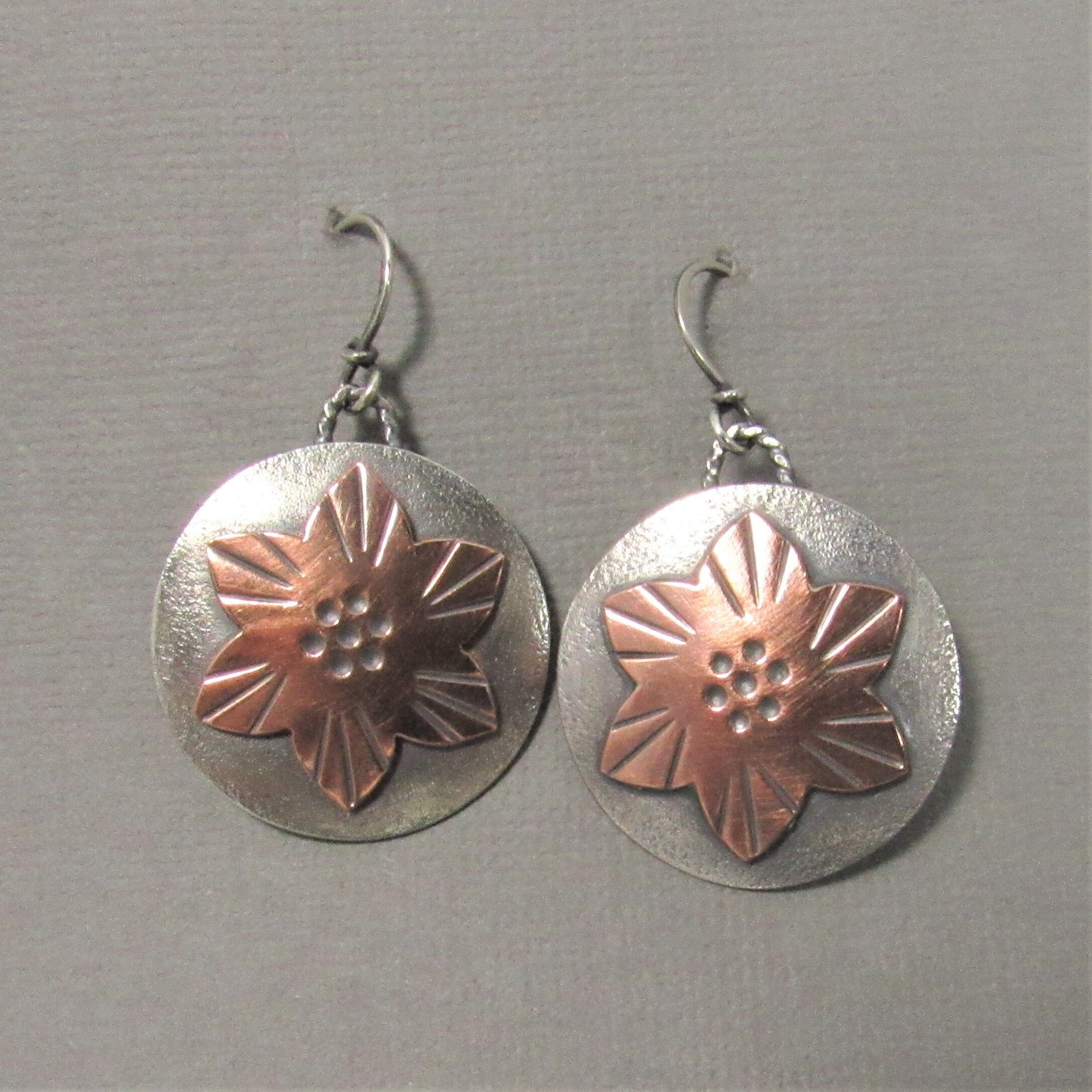 Mixed metal flower earrings handcrafted from copper and Argentium silver, lightly oxidized for depth and texture. On grey background.