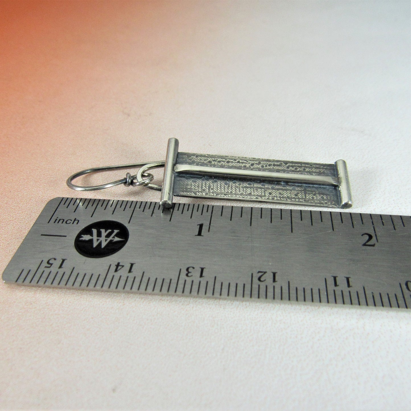 Linear earrings with texture and bars on a ruler for scale.