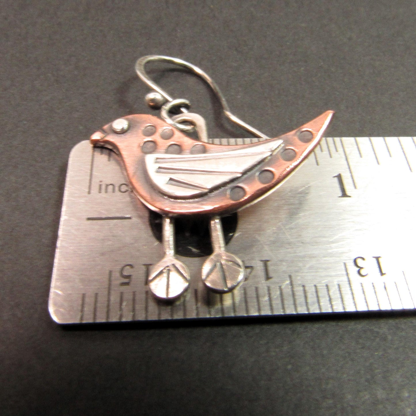 Copper and silver bird earrings on ruler.