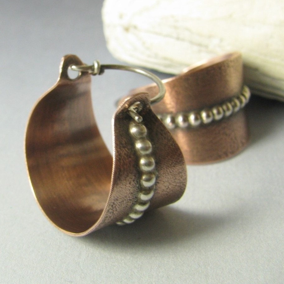 Copper hoop earrings with a textured band on a light gray background