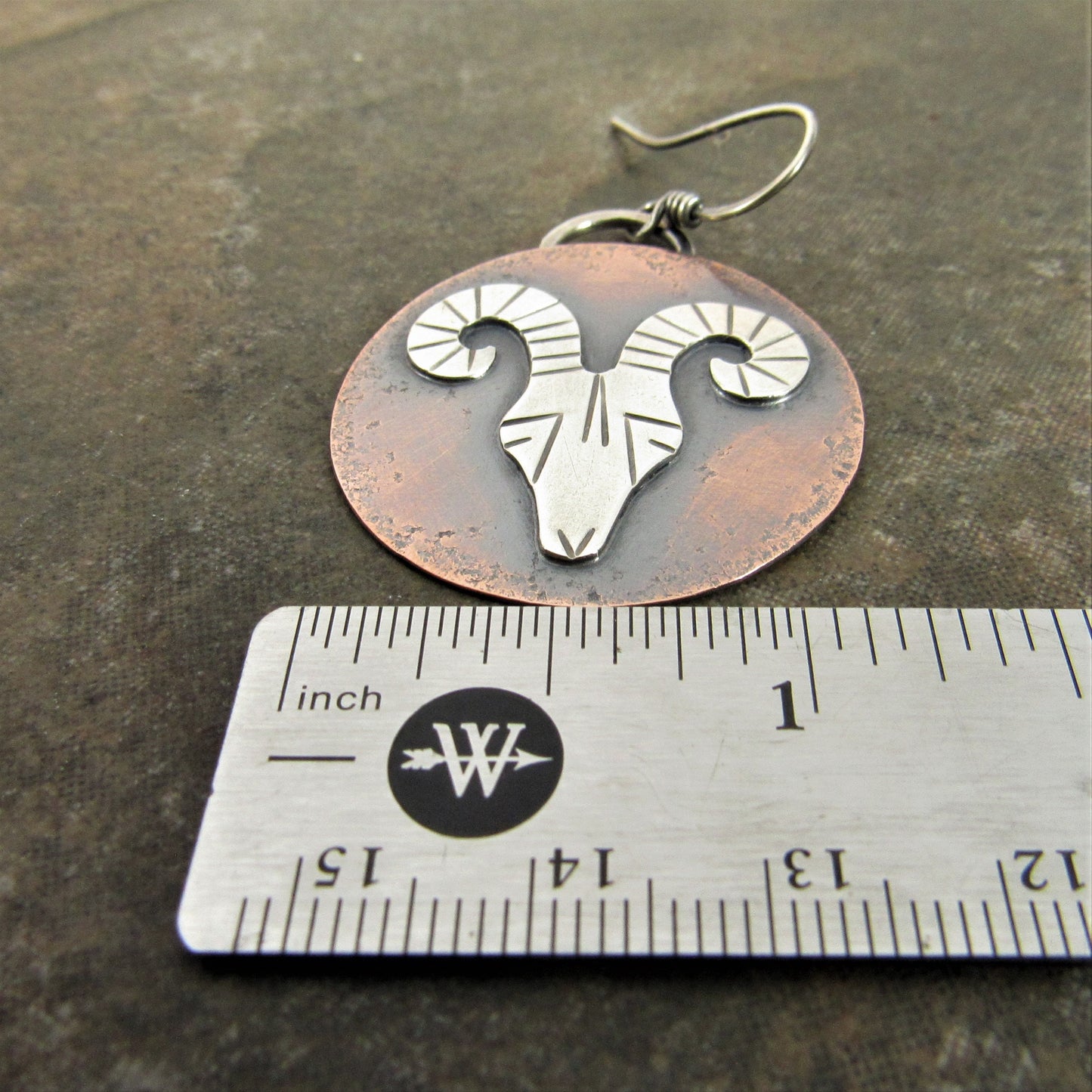 Rams head earrings on dark background with ruler.