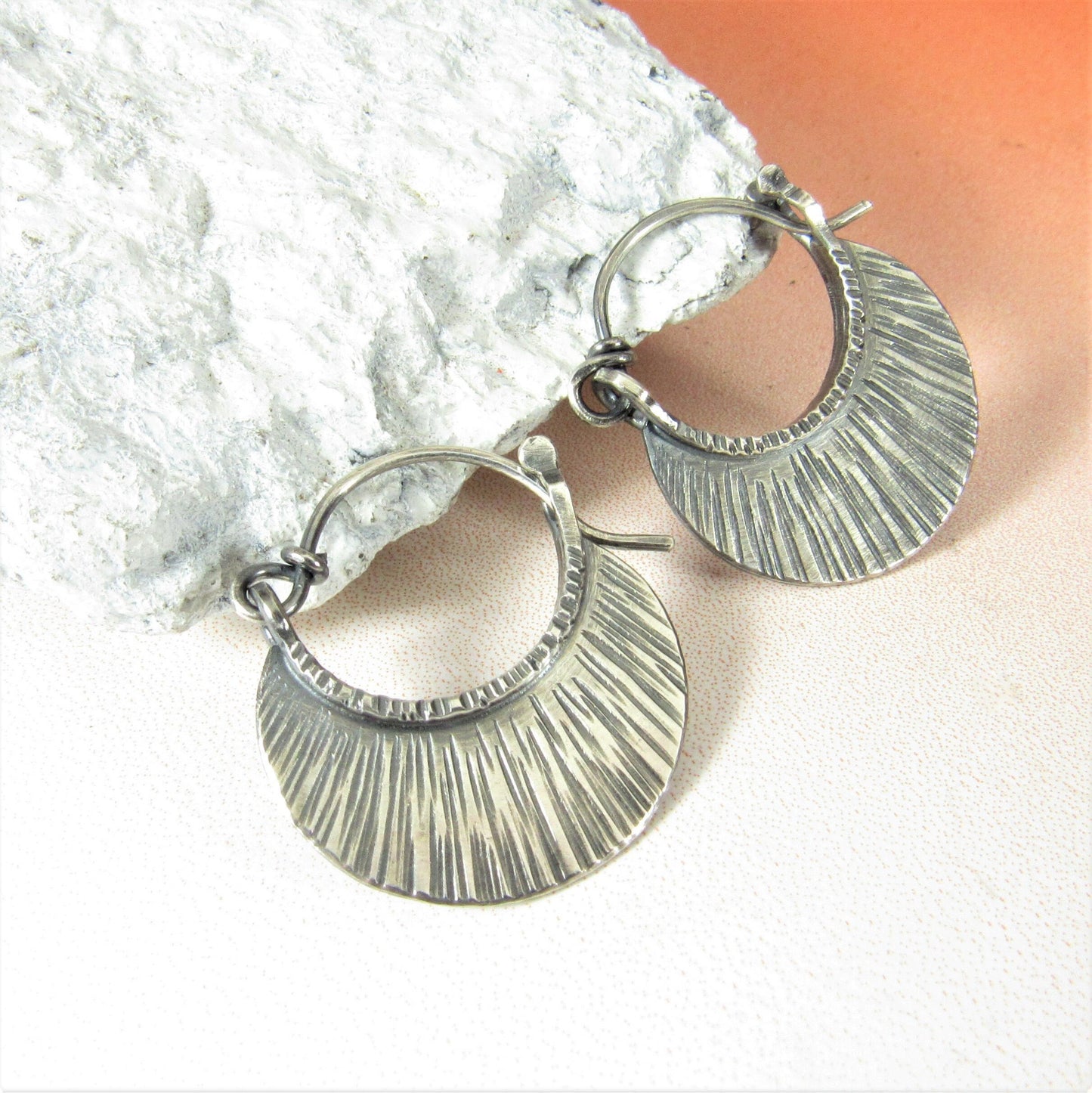Small textured argentium silver hoop earrings against white rock on orange background.