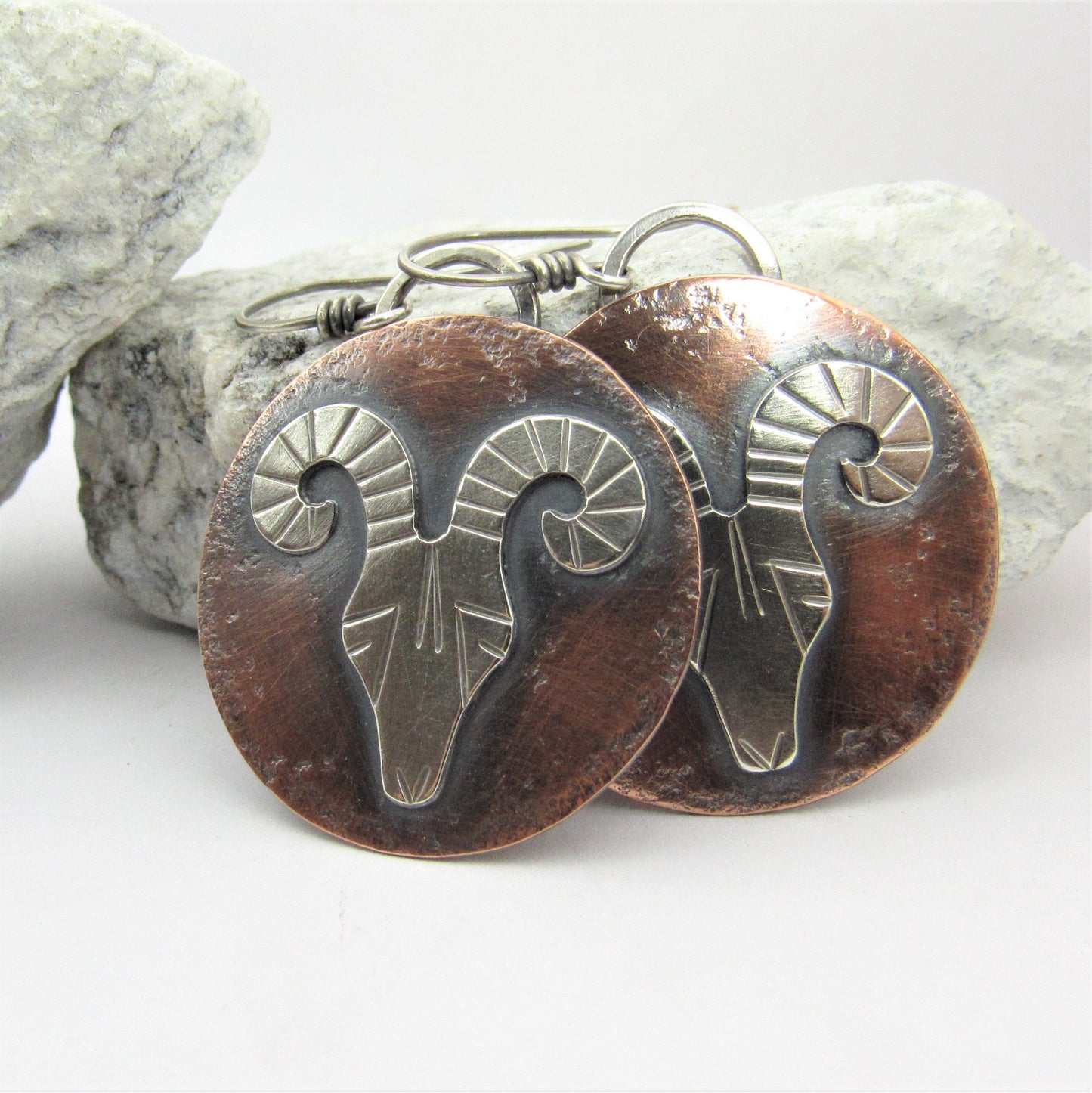 Copper and silver Rams head aries earrings on white background.