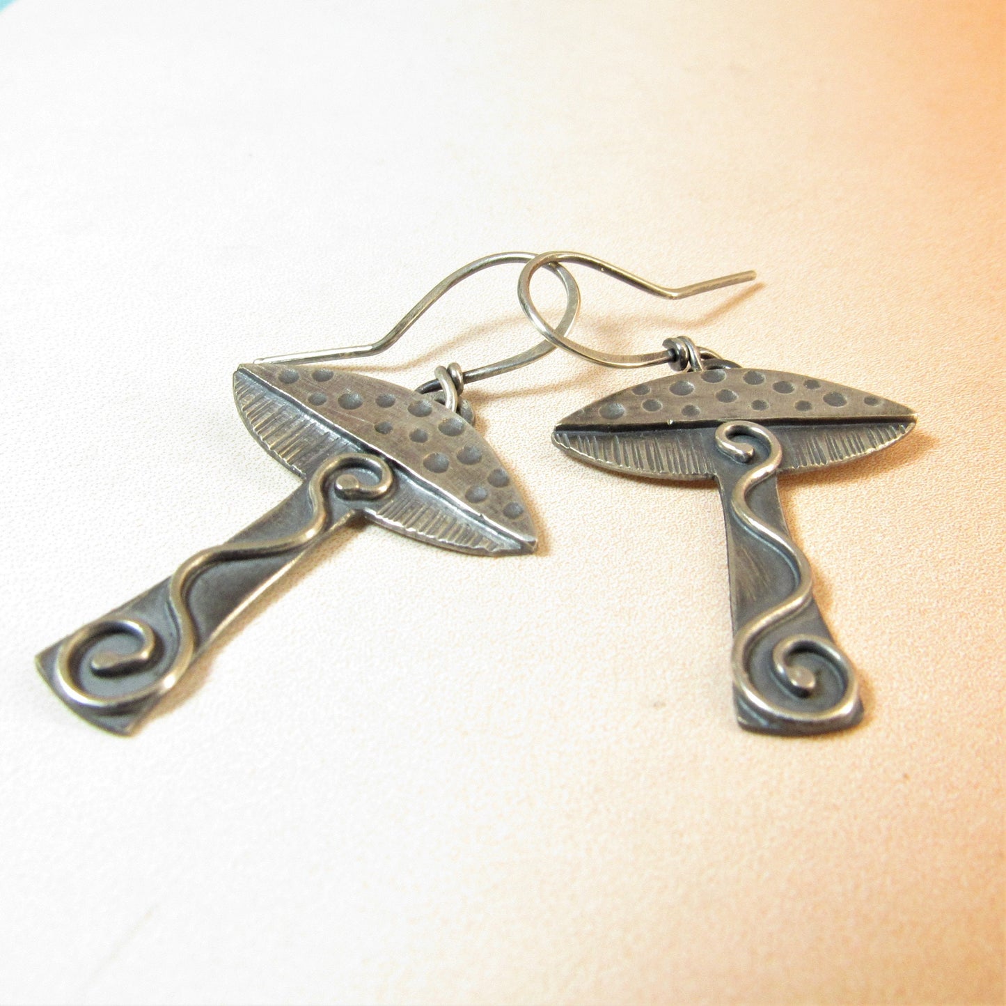 Mushroom earrings in argentium sterling silver by Mocahete on pale background.