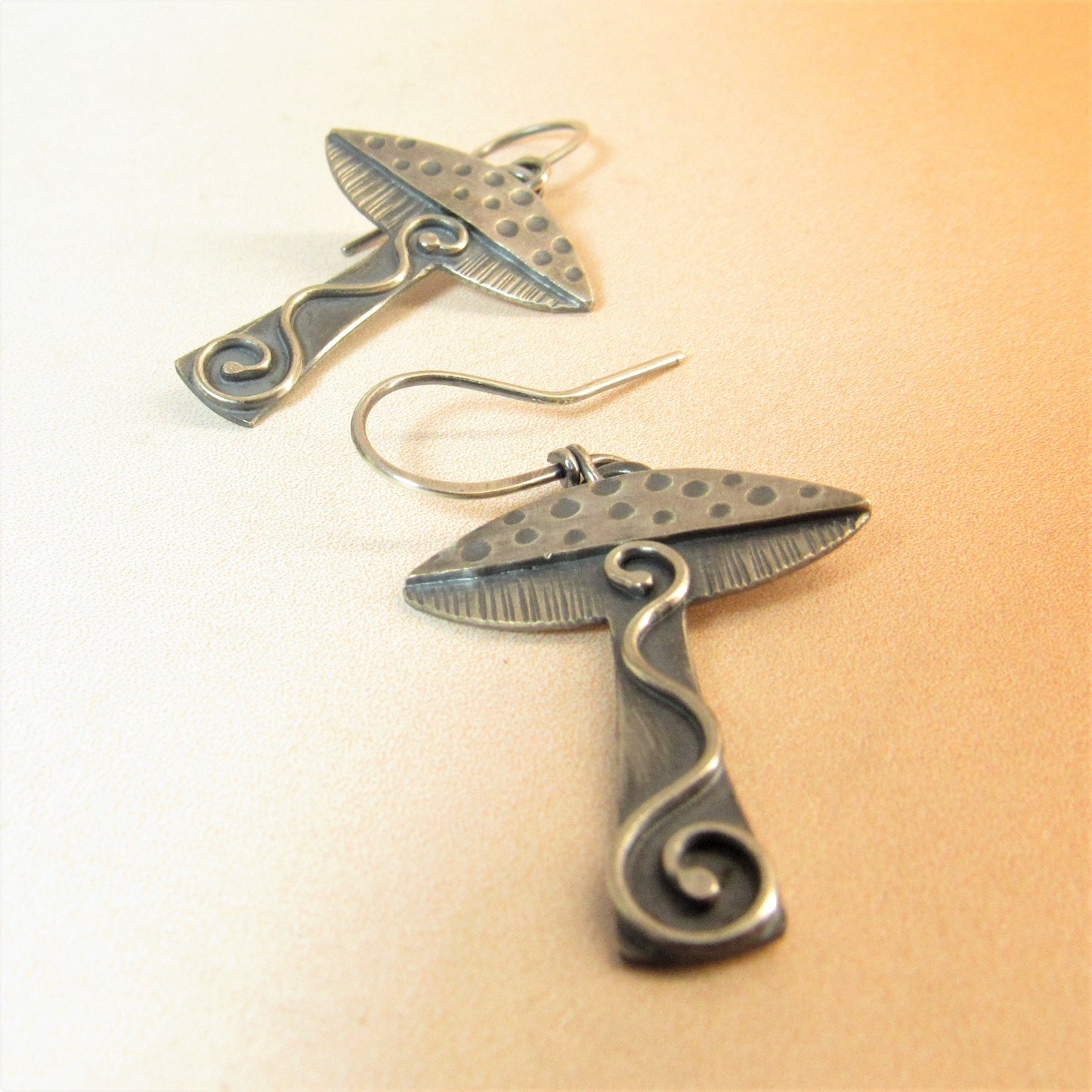 Artisan mushroom earrings in argentium silver on orange and white background