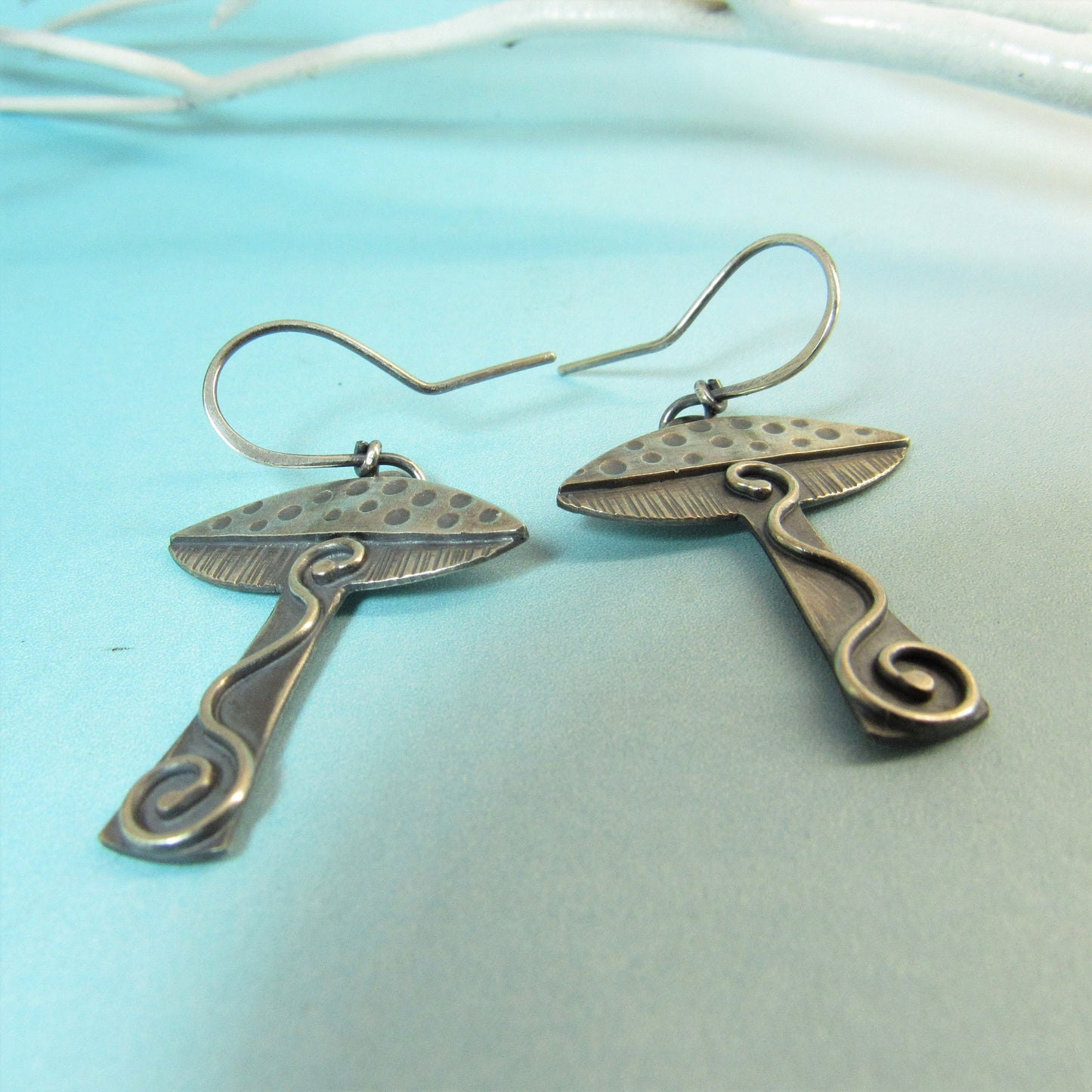 Artisan made mushroom dangle earrings on blue background.