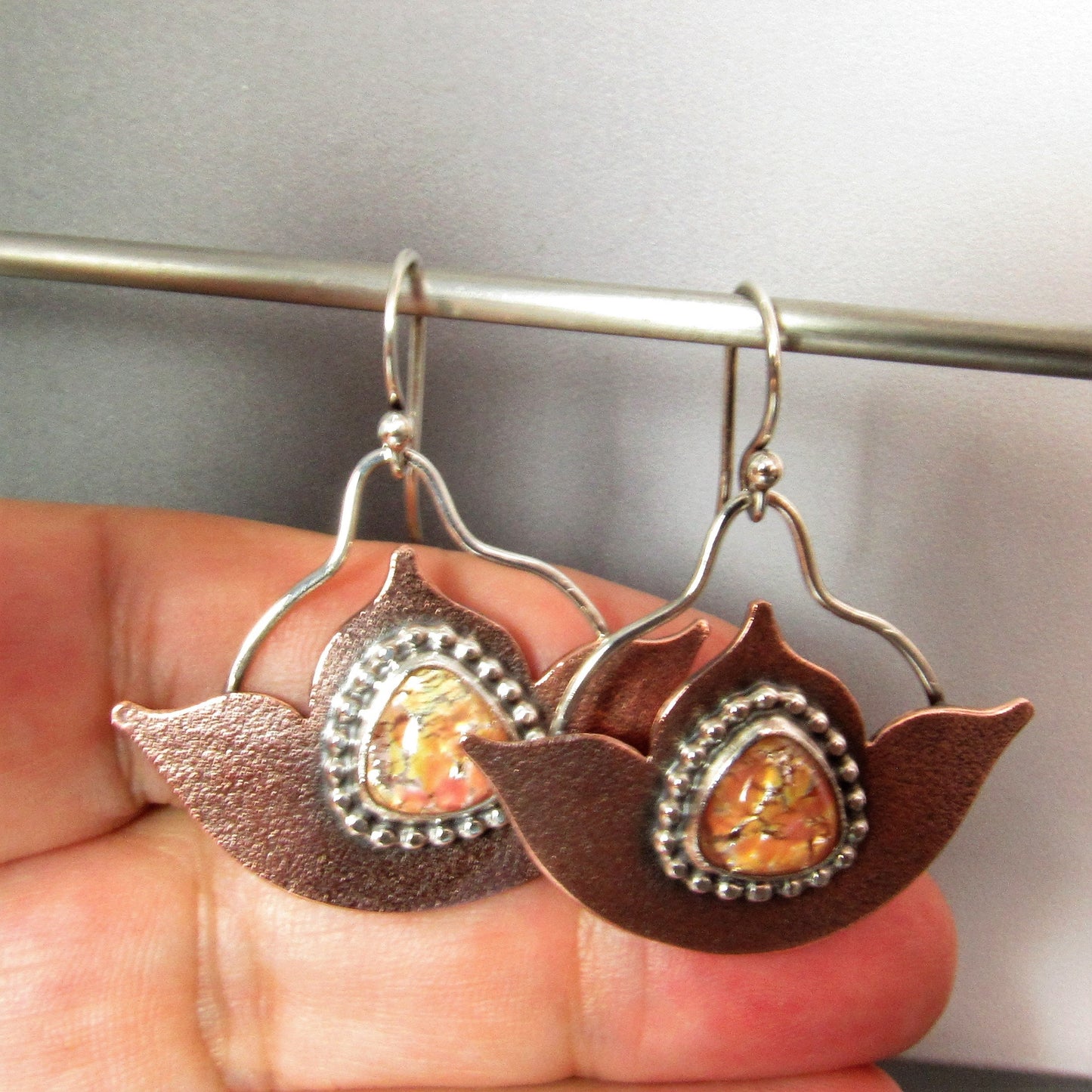 Photo of suspended earrings against hand. Mixed metal lotus earrings featuring glowing vintage glass opals, beaded sterling silver detailing, and Argentium silver ear wires.