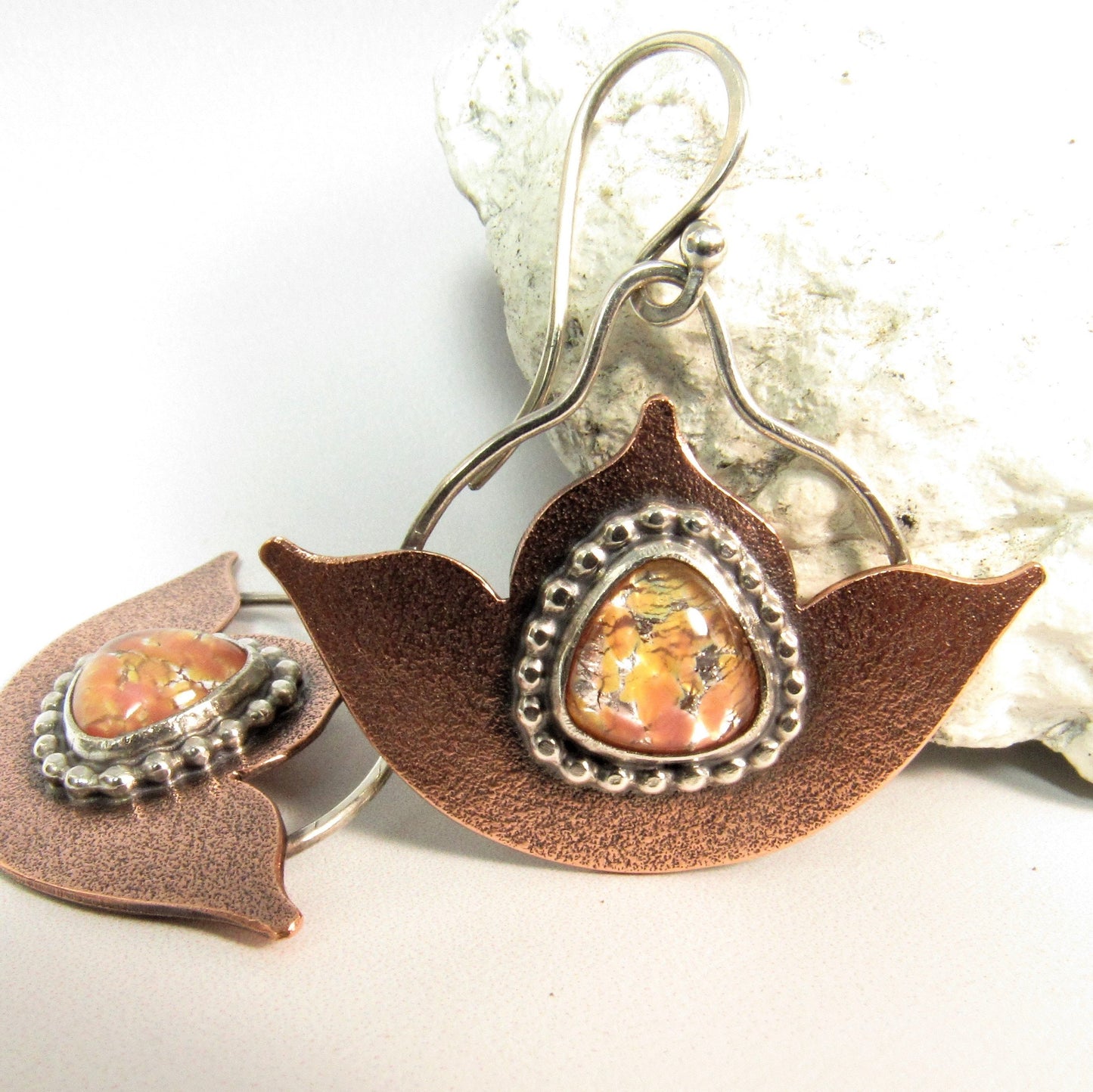 Handcrafted copper and silver lotus earrings with vintage golden pink glass opal cabochons from 1940s Japan, artisan made by Mocahete. Photo on white background with white rock as prop.