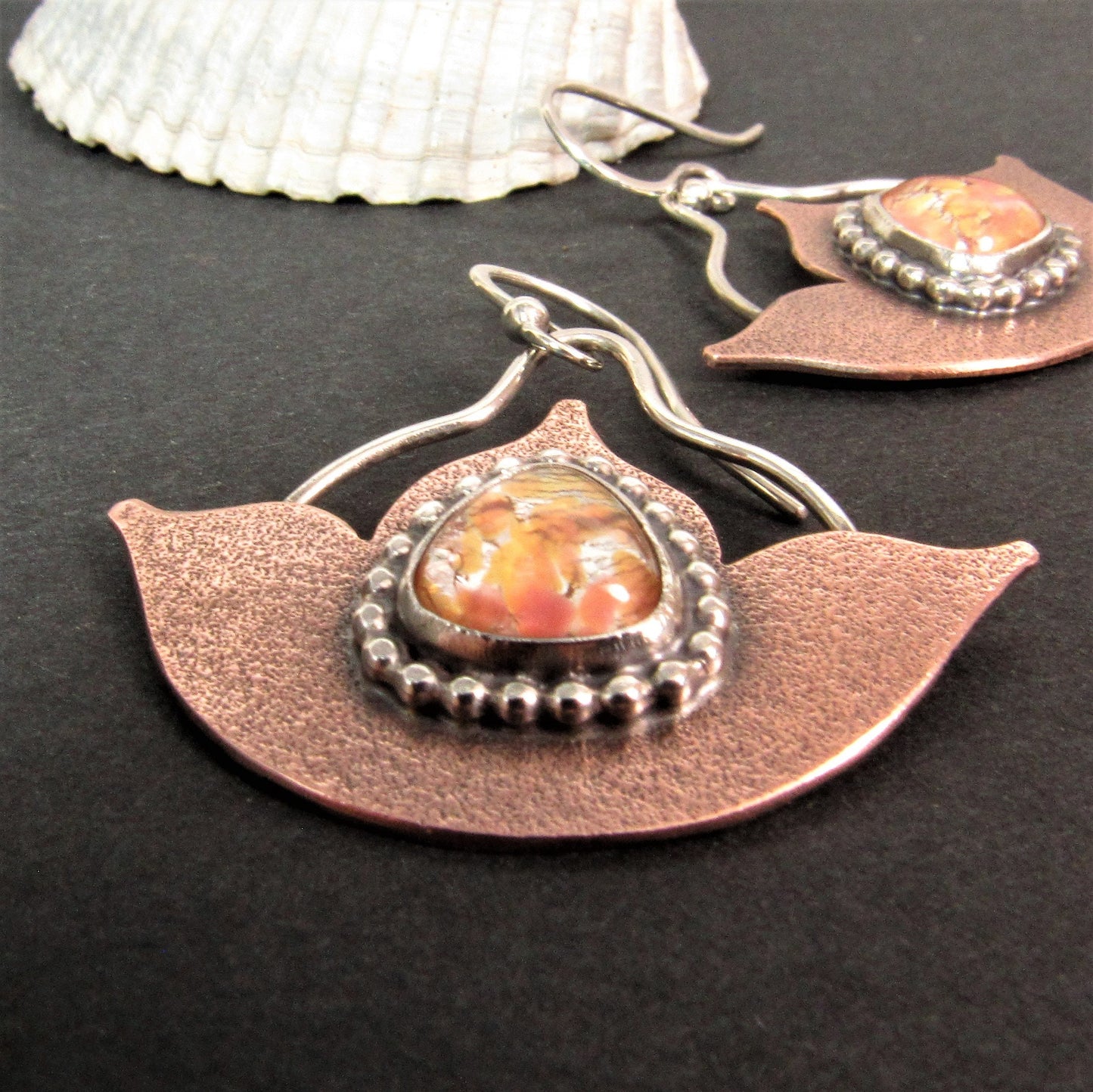 Mixed metal lotus earrings featuring glowing vintage glass opals, beaded sterling silver detailing, and Argentium silver ear wires. Photo on dark background with white shell as prop.