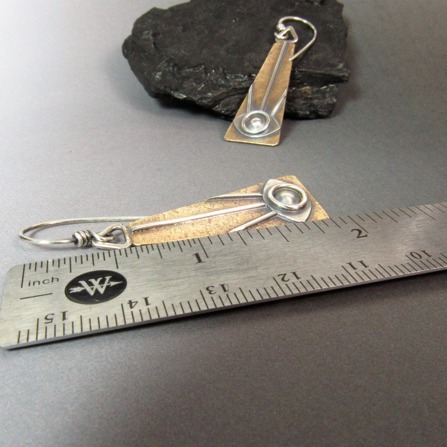 Handcrafted bronze and silver seeing eye earrings with rustic finish shown against ruler